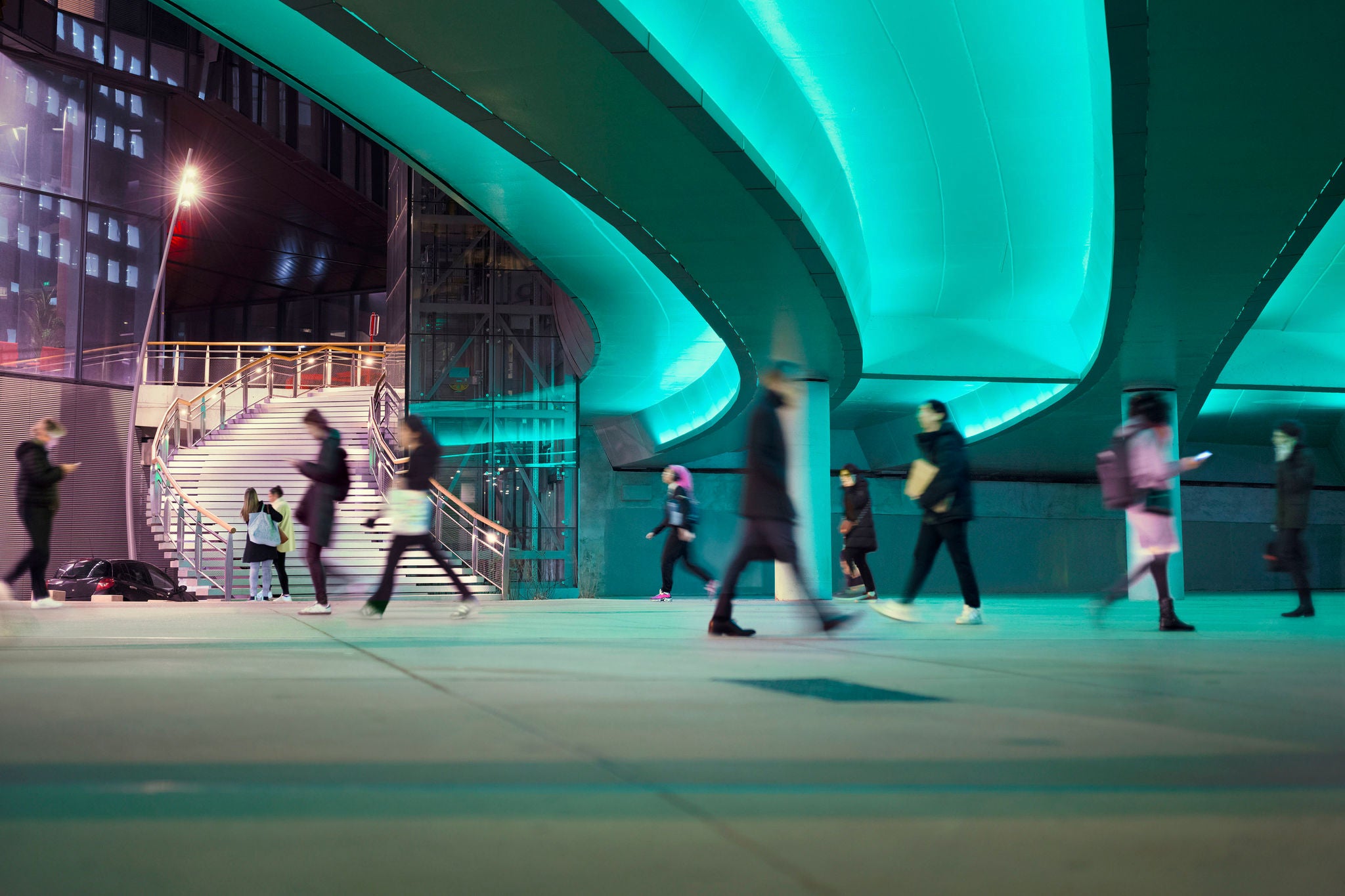 Evening commute with office workers and business people passing a LED illuminated viaduct at La Defense business district in Paris, France.