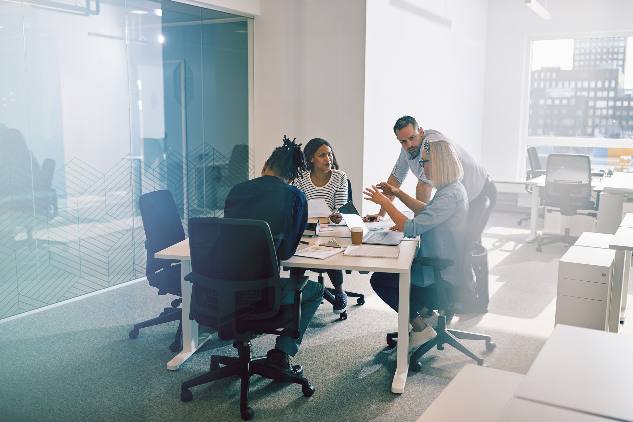 Diverse groep collega's bespreekt zaken in een kantoor met glazen wanden