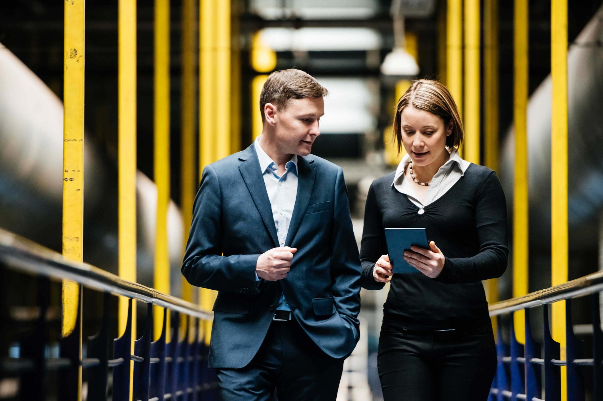 Two Business Person Walking A Dark Factory Hallway and talking about their latest projects