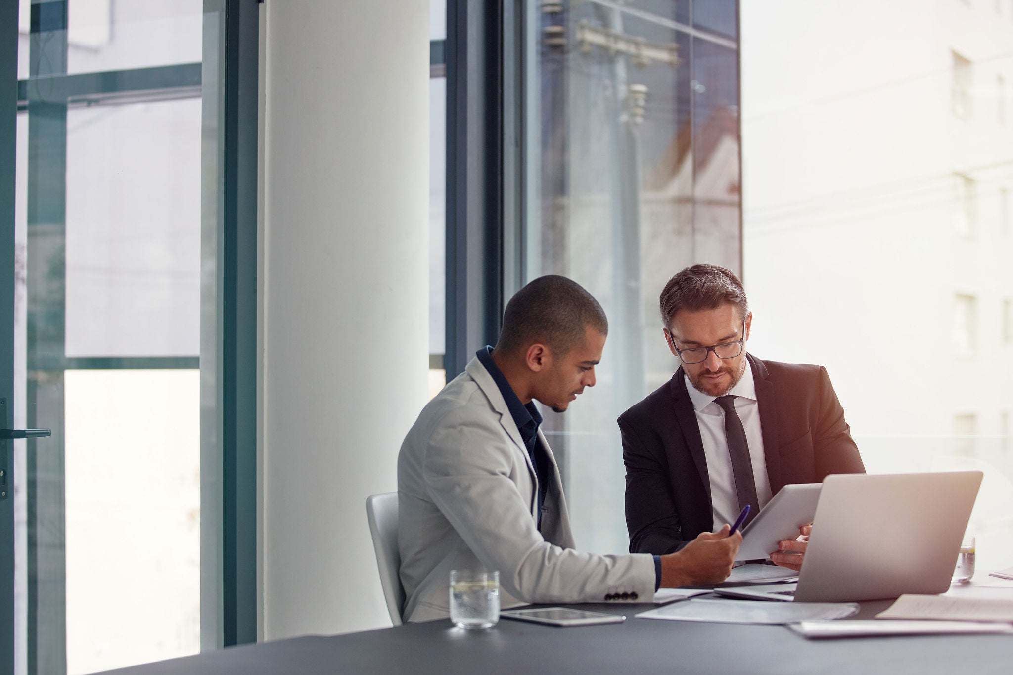 Tablet, laptop and business men planning in conference room meeting, teamwork and discussion of corporate data. Professional people or partner talking, review or report analysis on digital technology.