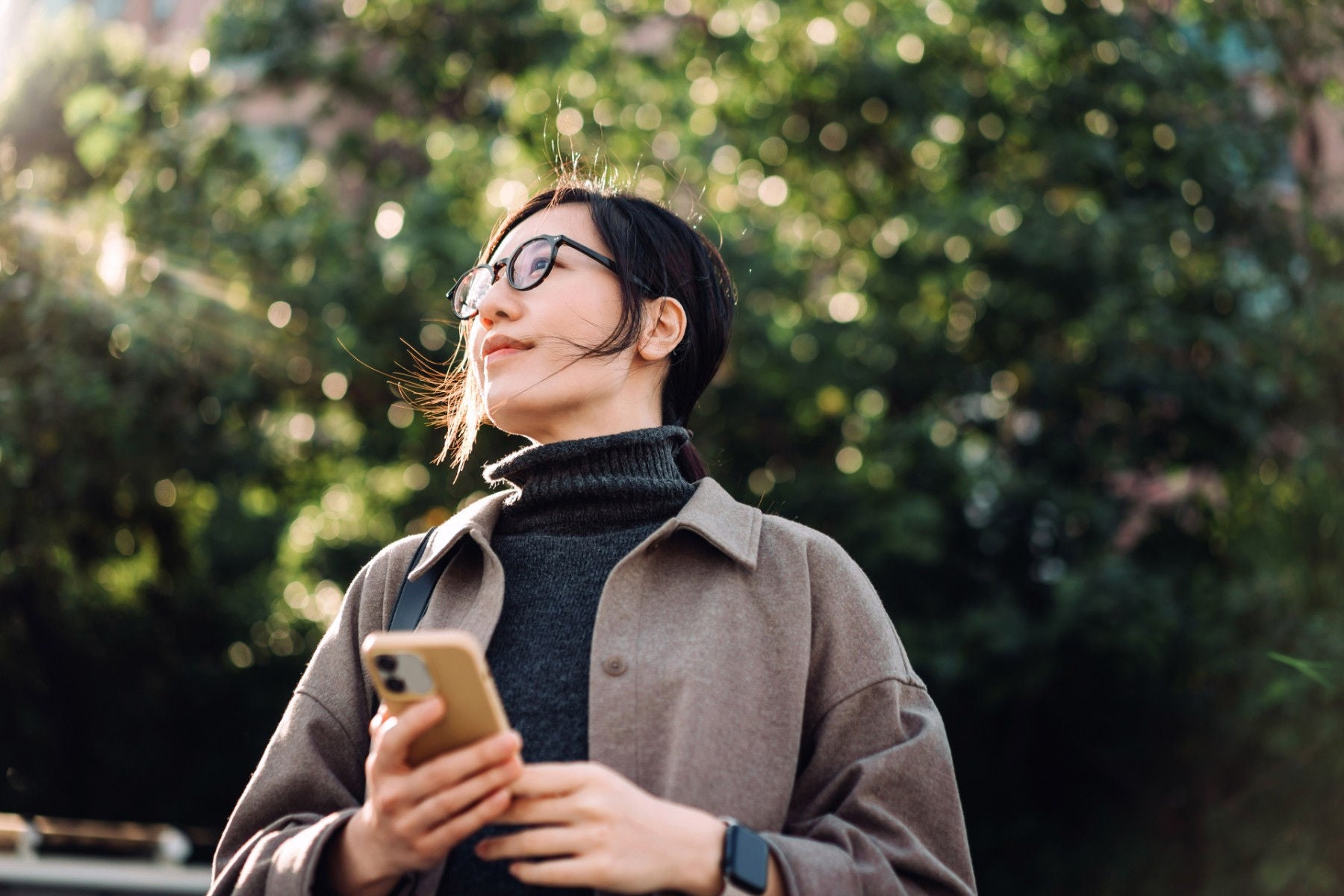 low-angle-portrait-of-young-asian-woman-using-smartphone-in-park-against-sunlight.