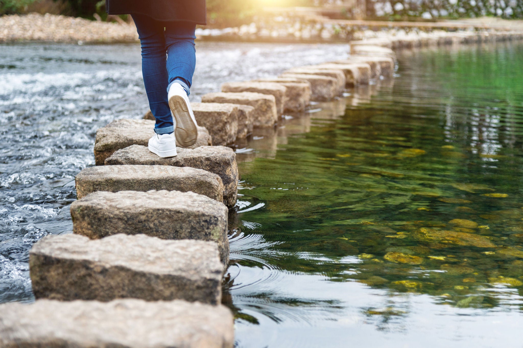 Woman crossing a river on stepping stones.