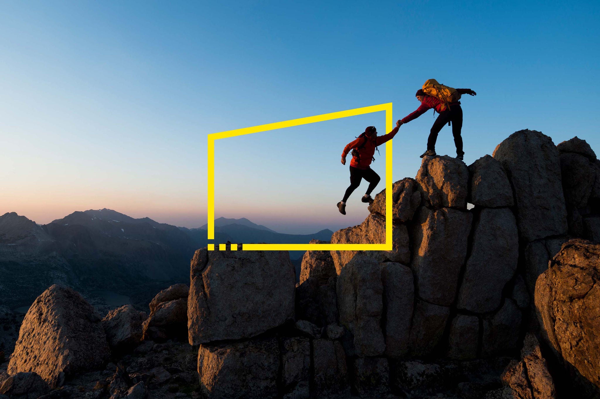 One climber helping the other get to the top of a mountain 