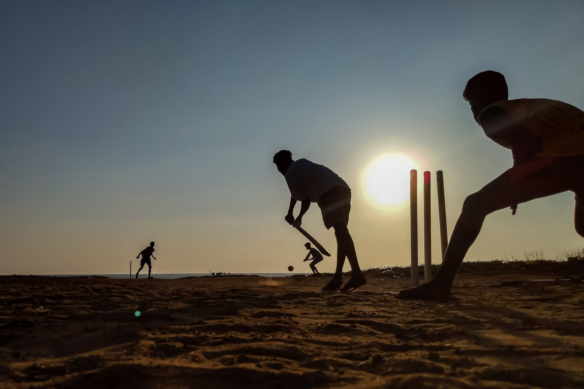 Silhouette of men playing cricket on a beach at sunset