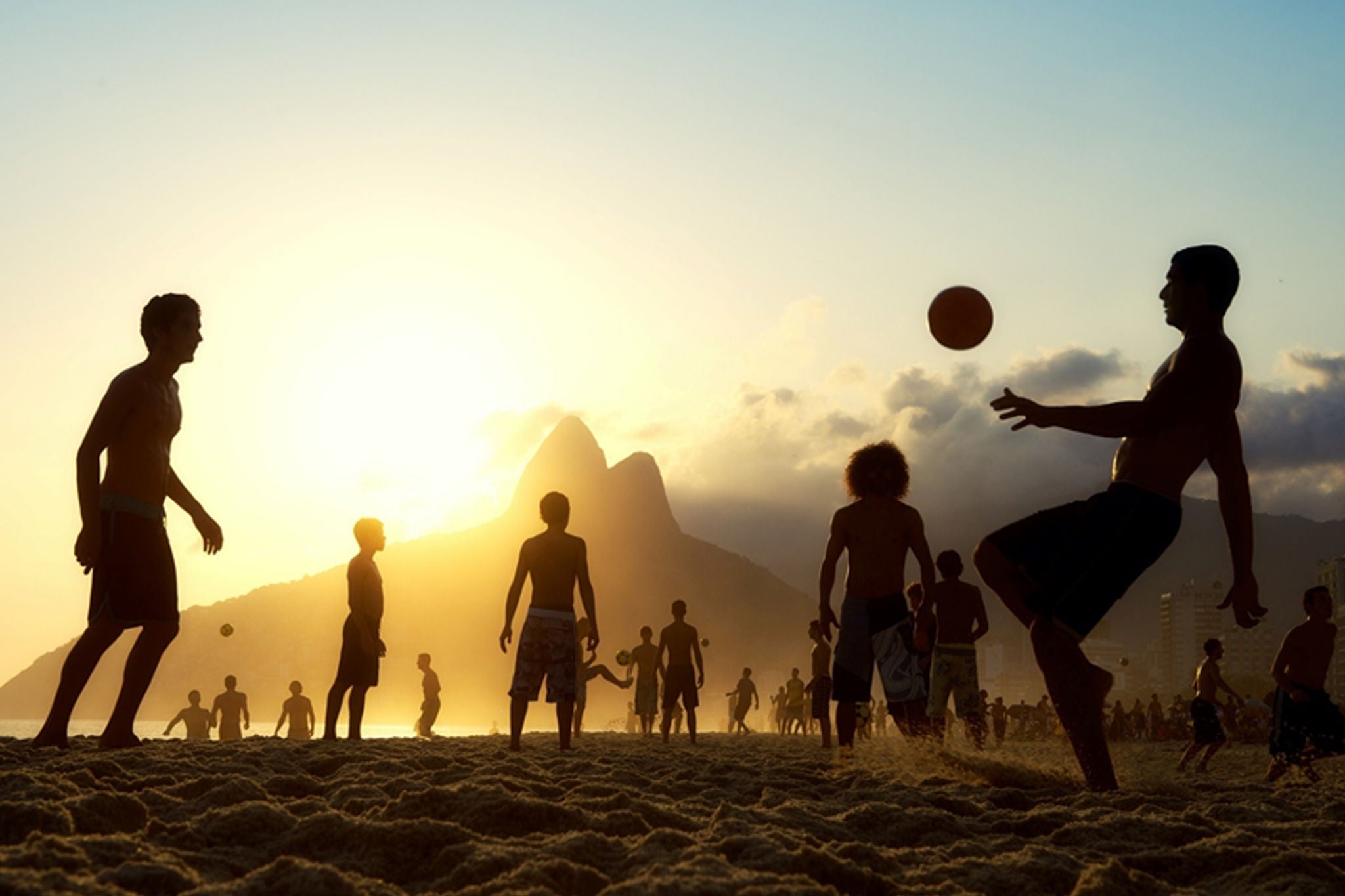 Homens jogando futebol na praia ao pôr do sol