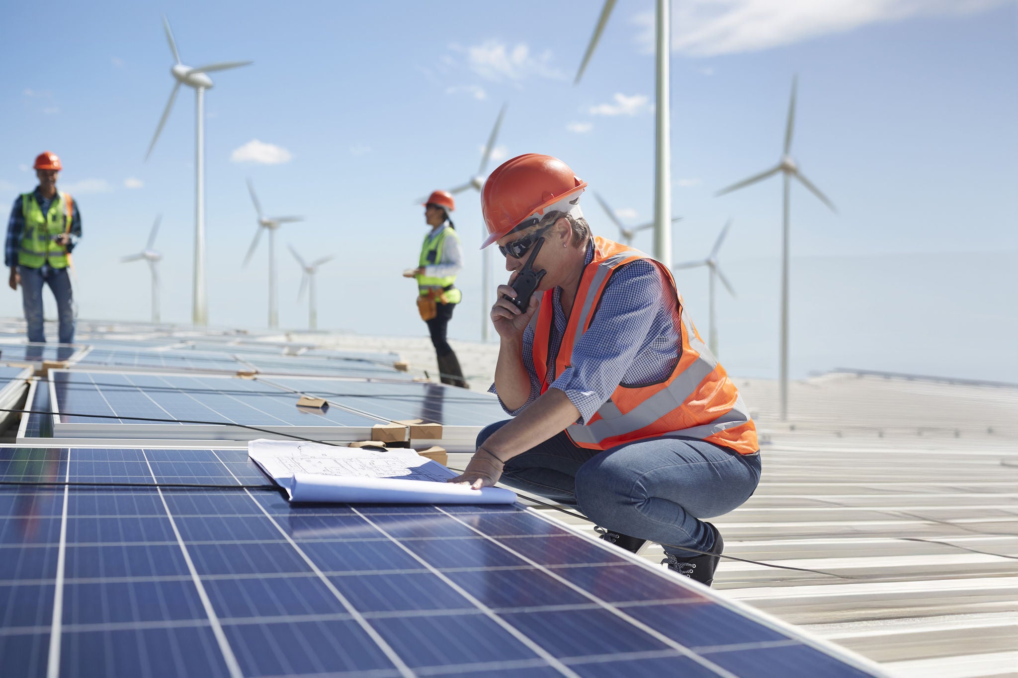 Engineer with walkie-talkie and blueprint at solar panel at sunny power plant