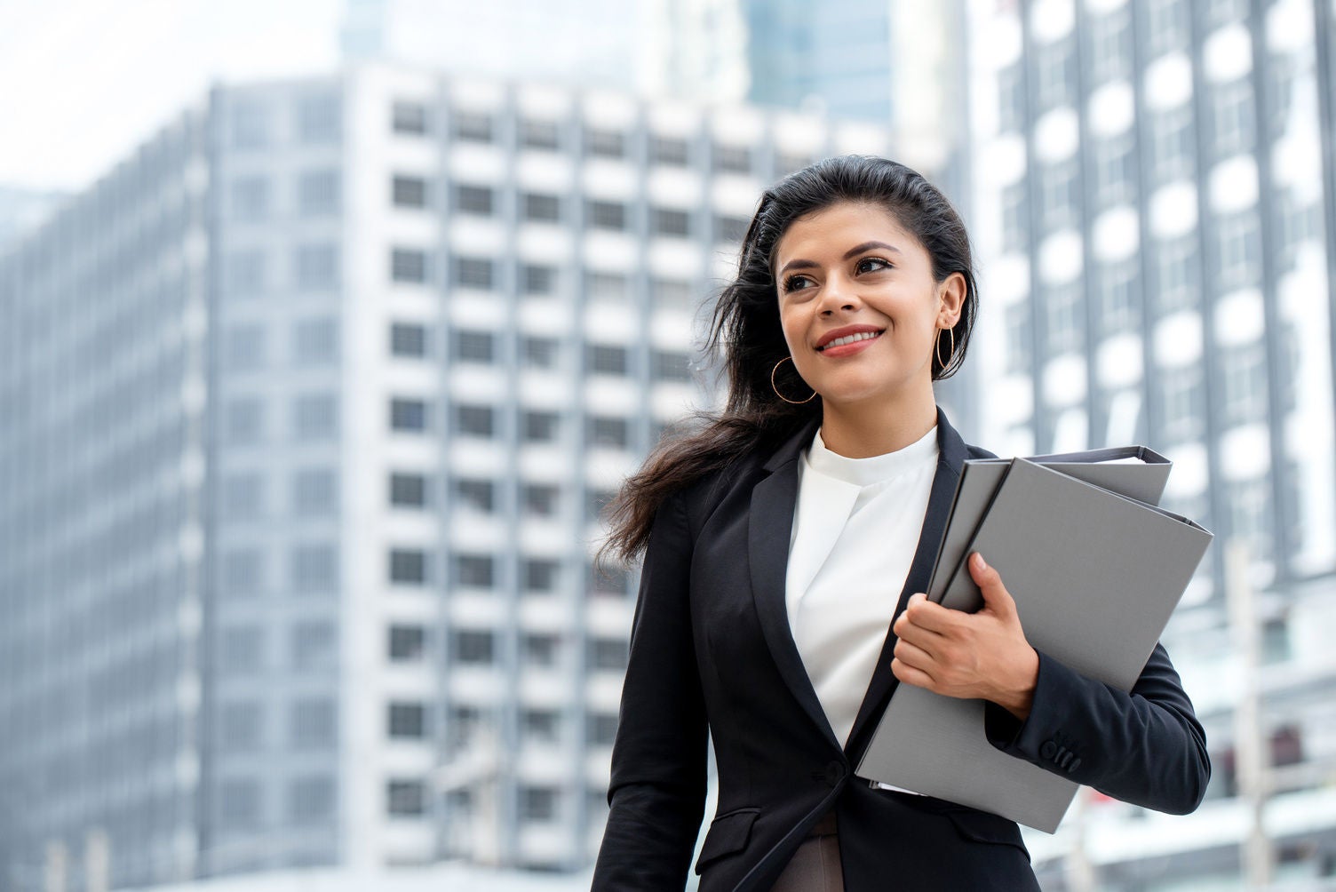 Young beautiful Latino businesswoman standing outdoors in city office building background