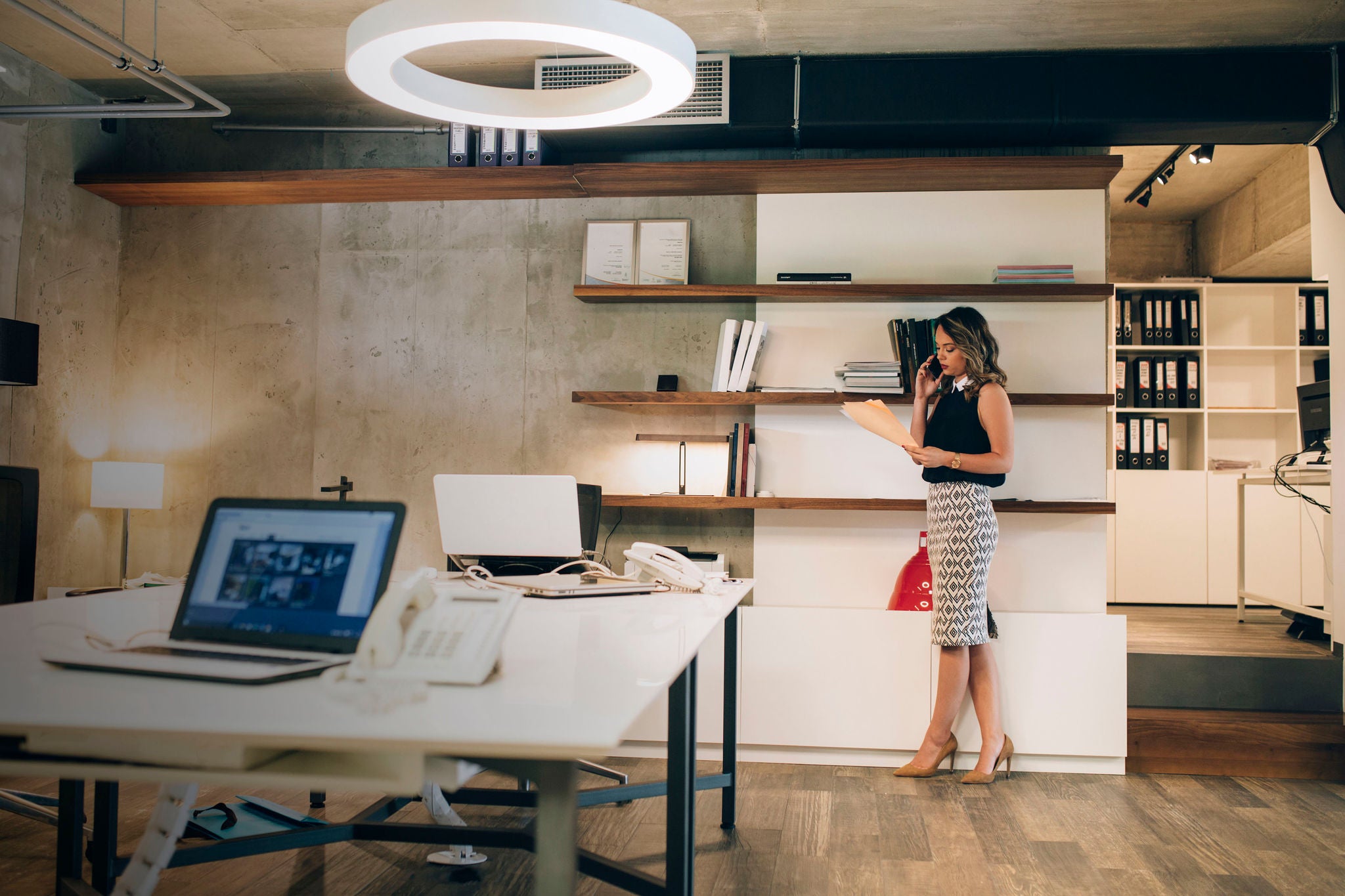 Businesswoman holding file and talking on smart phone in office