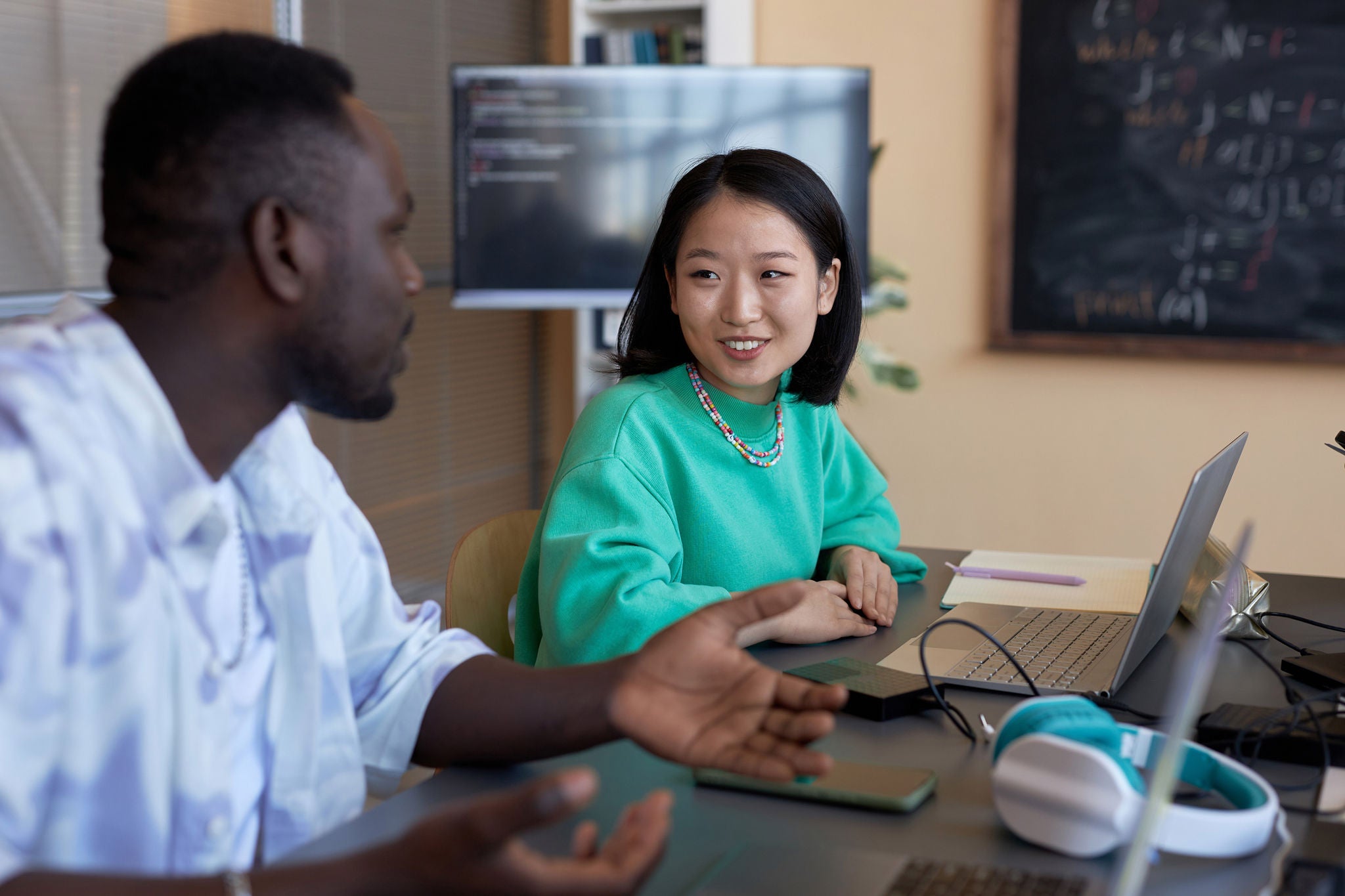 Happy Asian female student looking at African American classmate explaining her point of informatics project during discussion