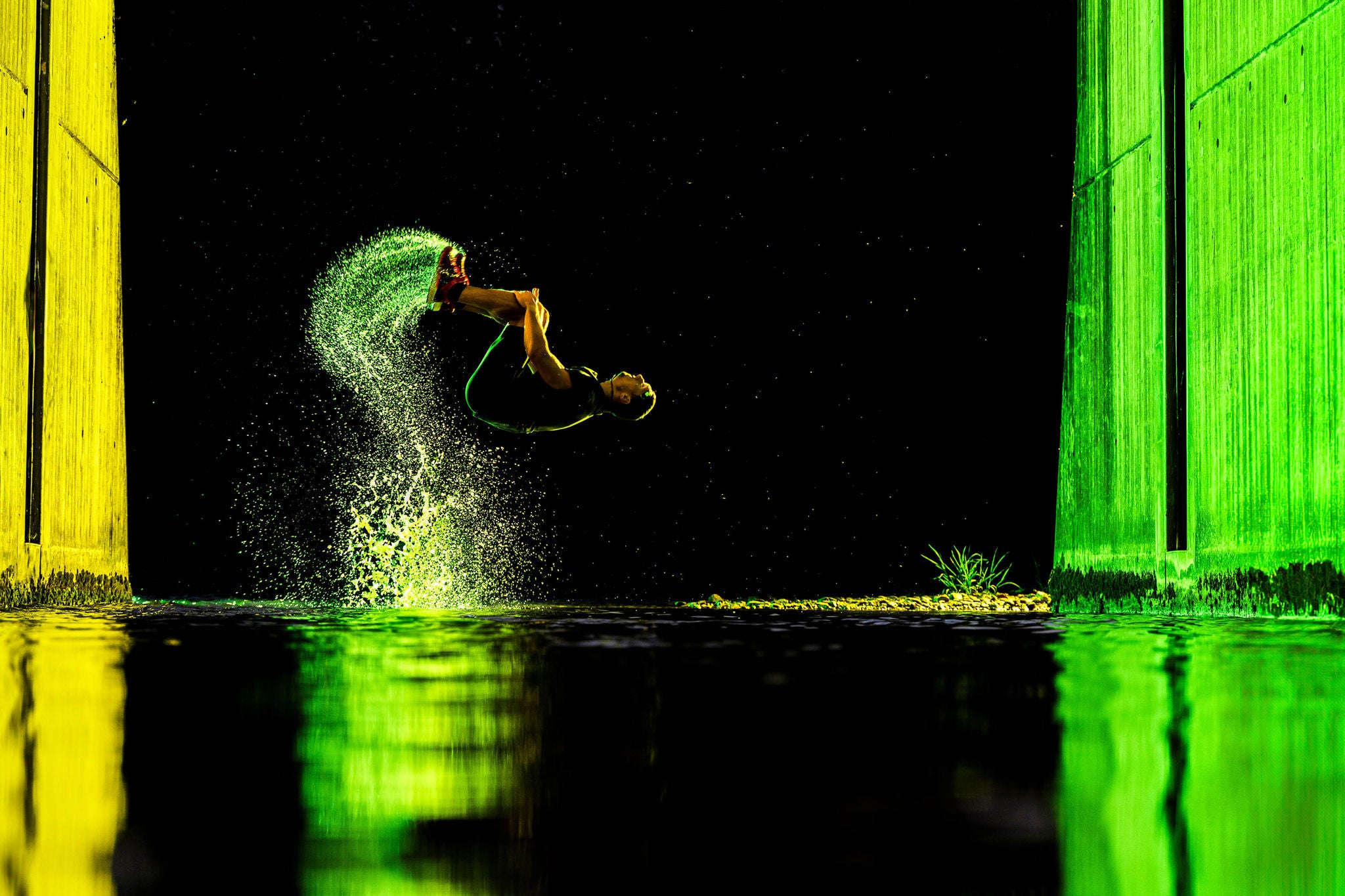 Young man backflipping with water under bridge at night