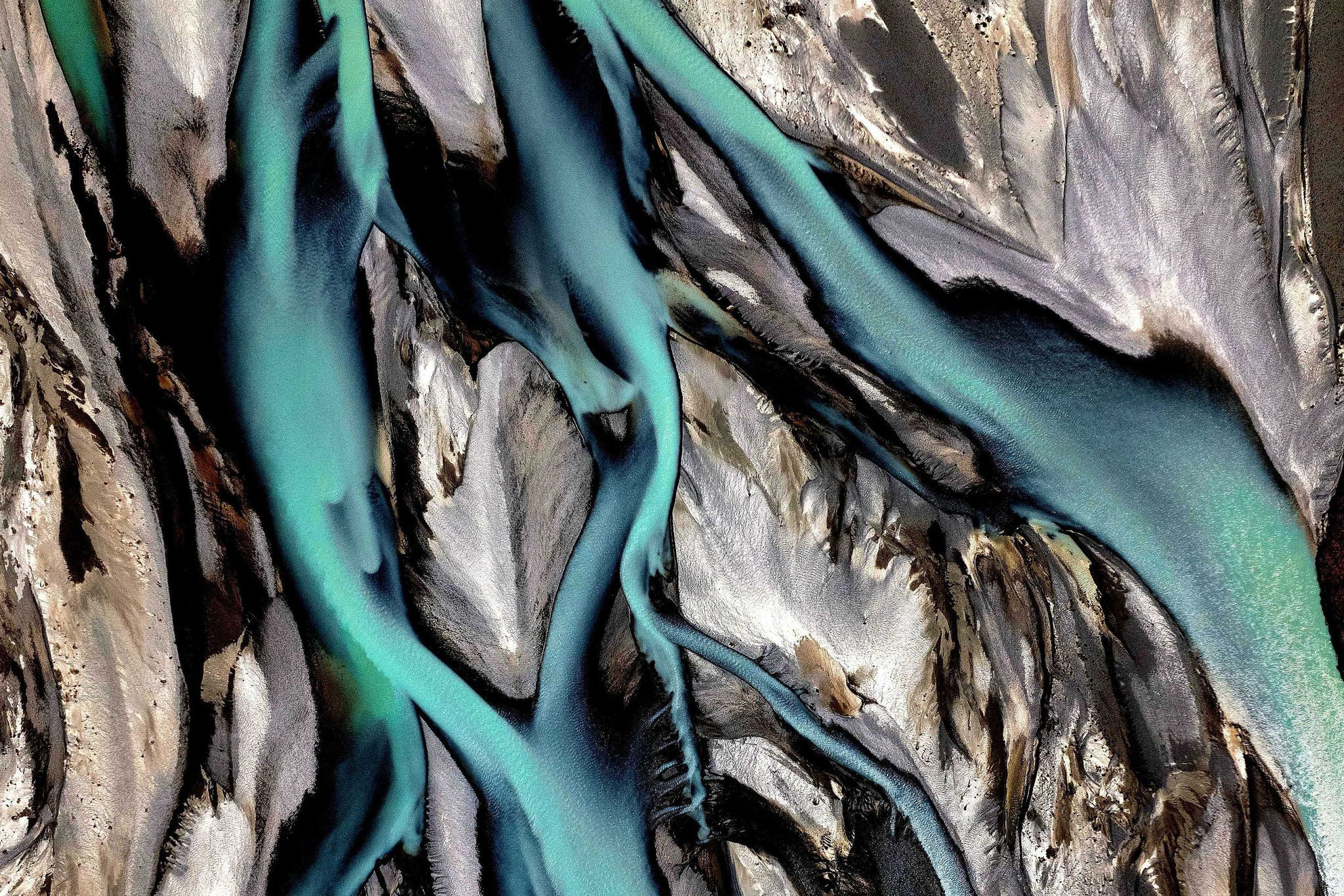 Aerial view of a braided river with vivid turquoise water flowing between dark and light sediment channels