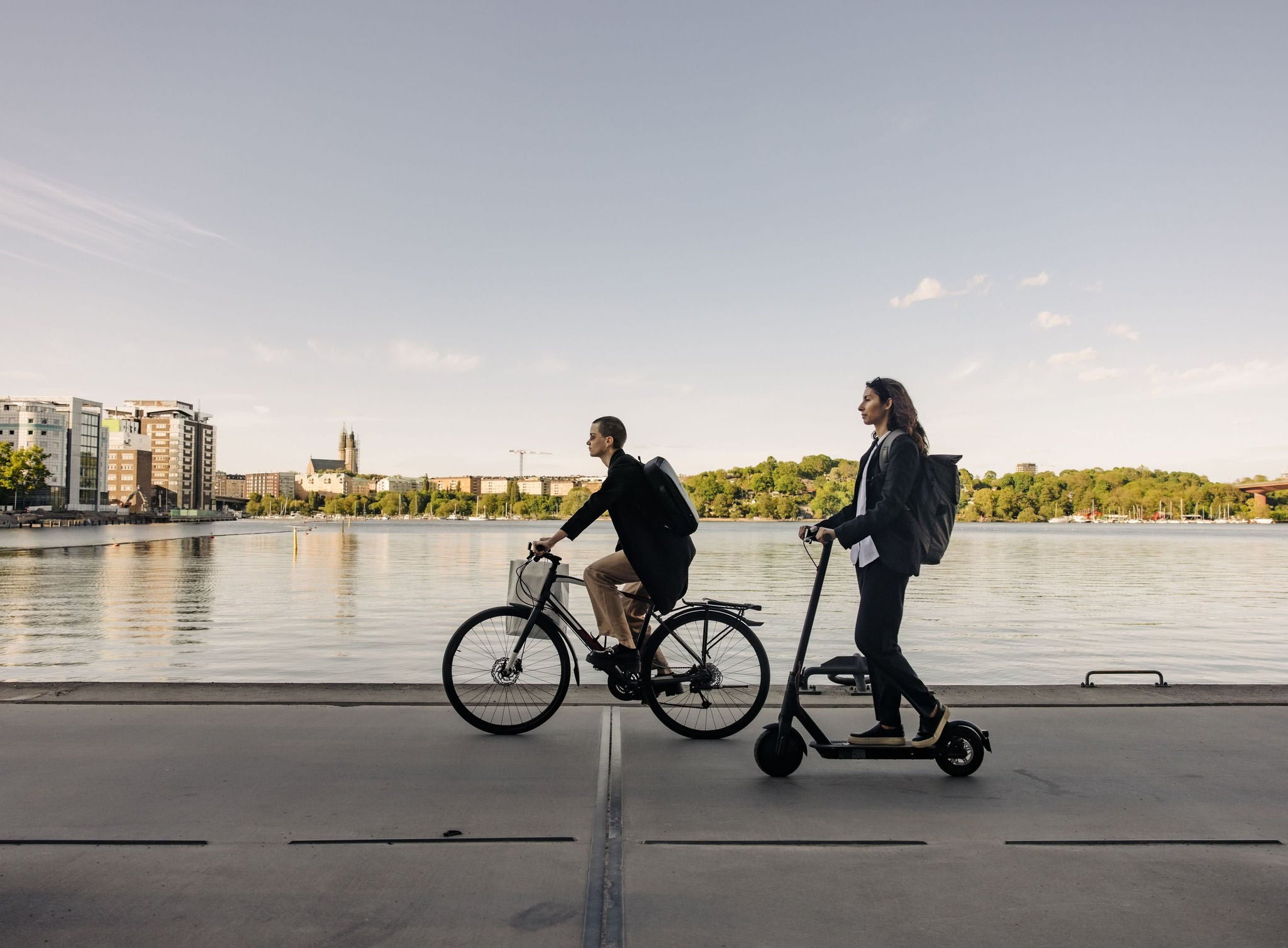 Business people riding electric scooter and bicycle on promenade against sky