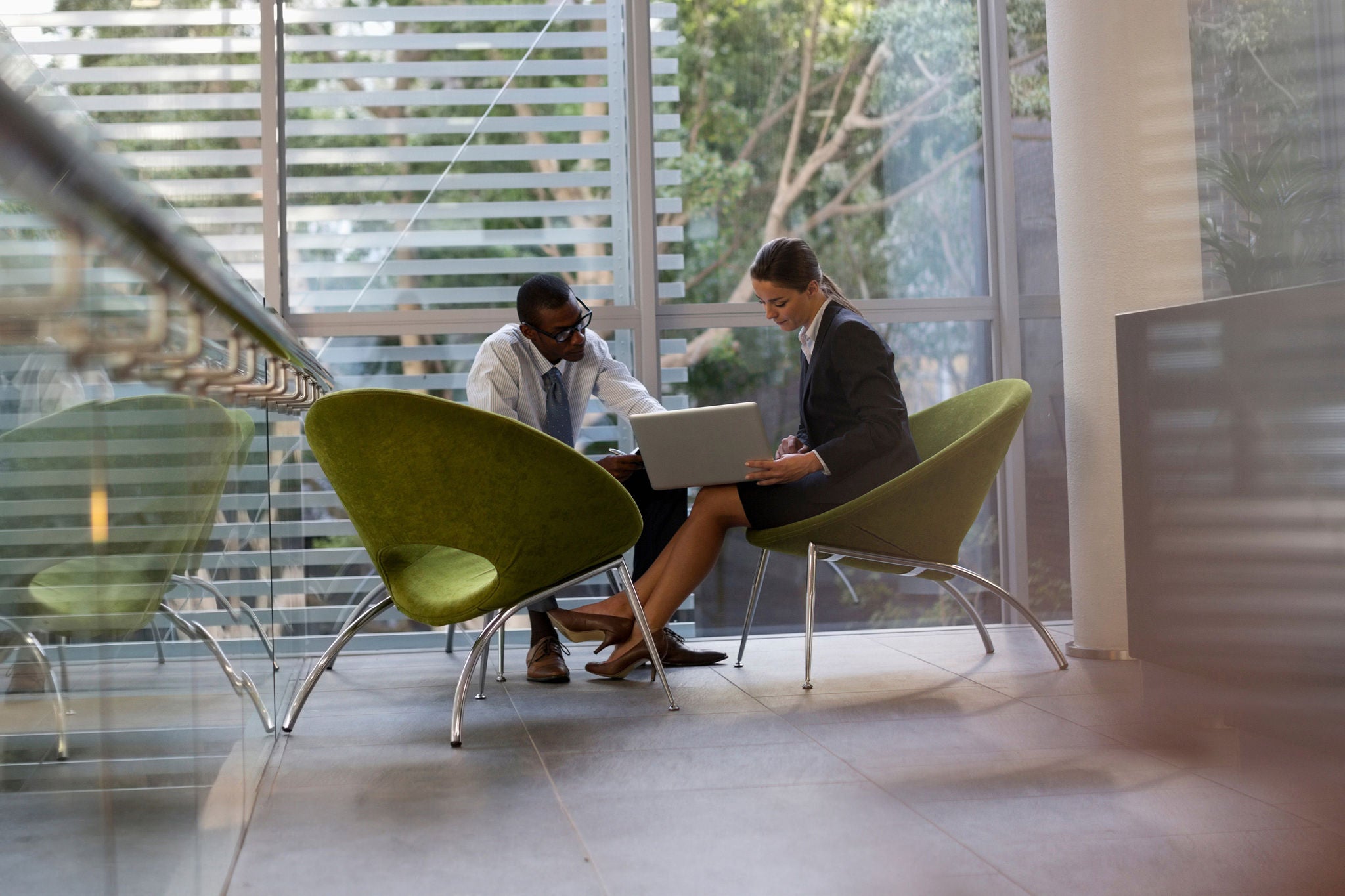 A businessman and businesswoman work on a laptop together in a lobby.






