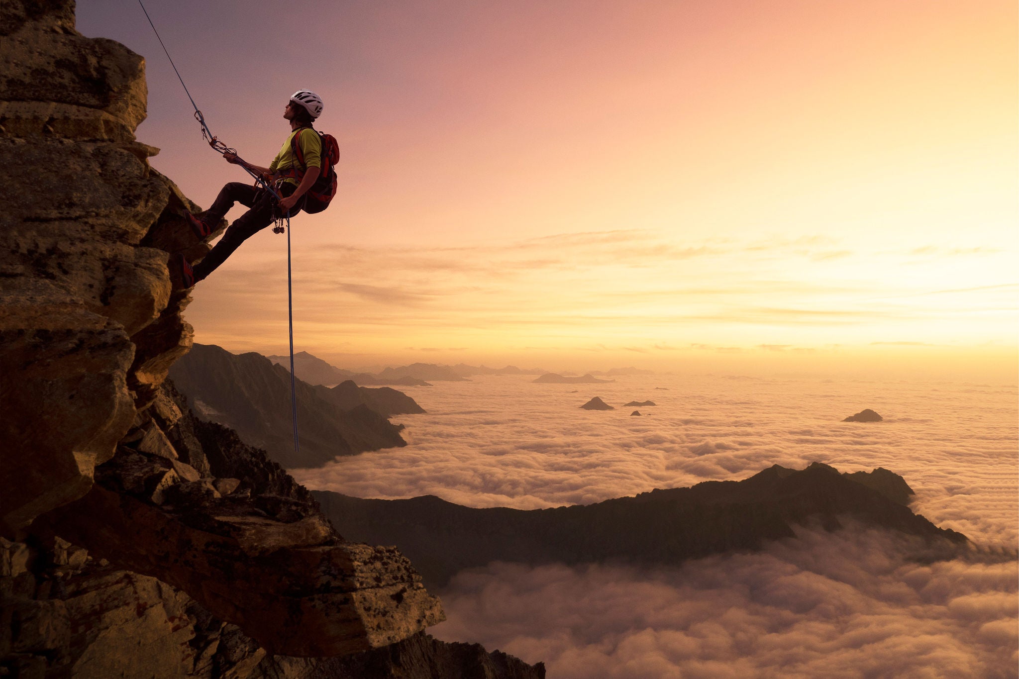 A climber on a rocky wall over clouds in the valley below at dawn