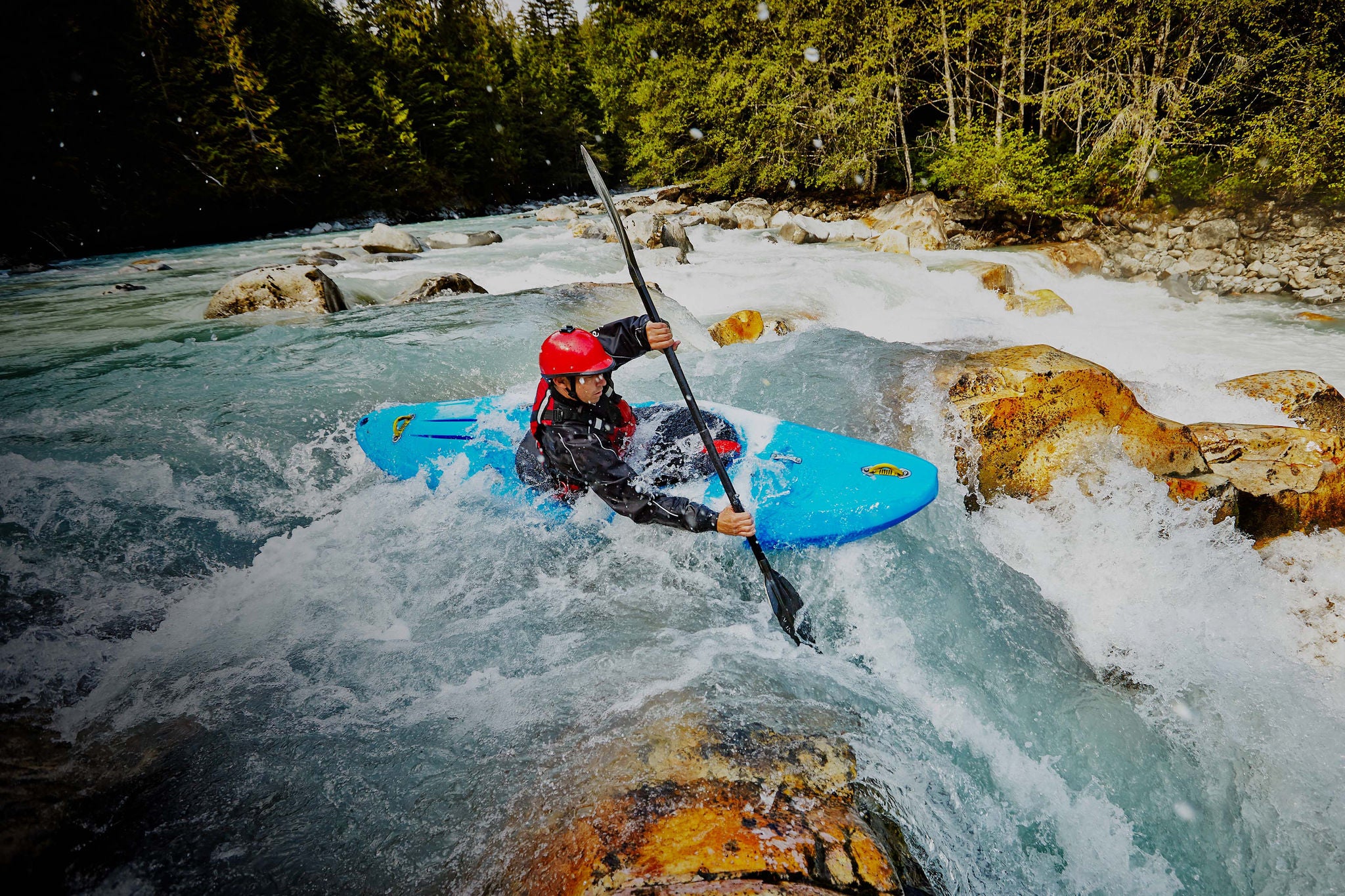 Kayaker entering white water rapids between narrow gap in rocks