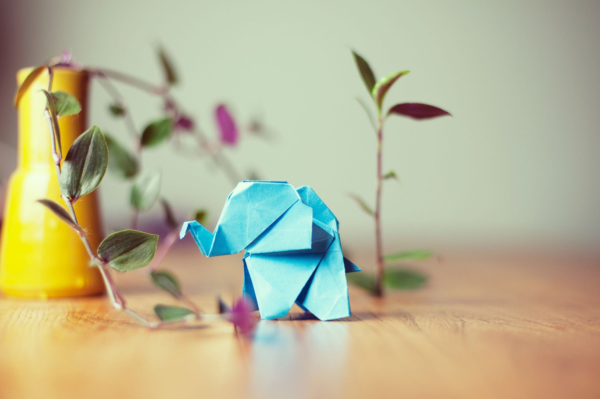 A blue origami elephant on a table with a plant next to it.