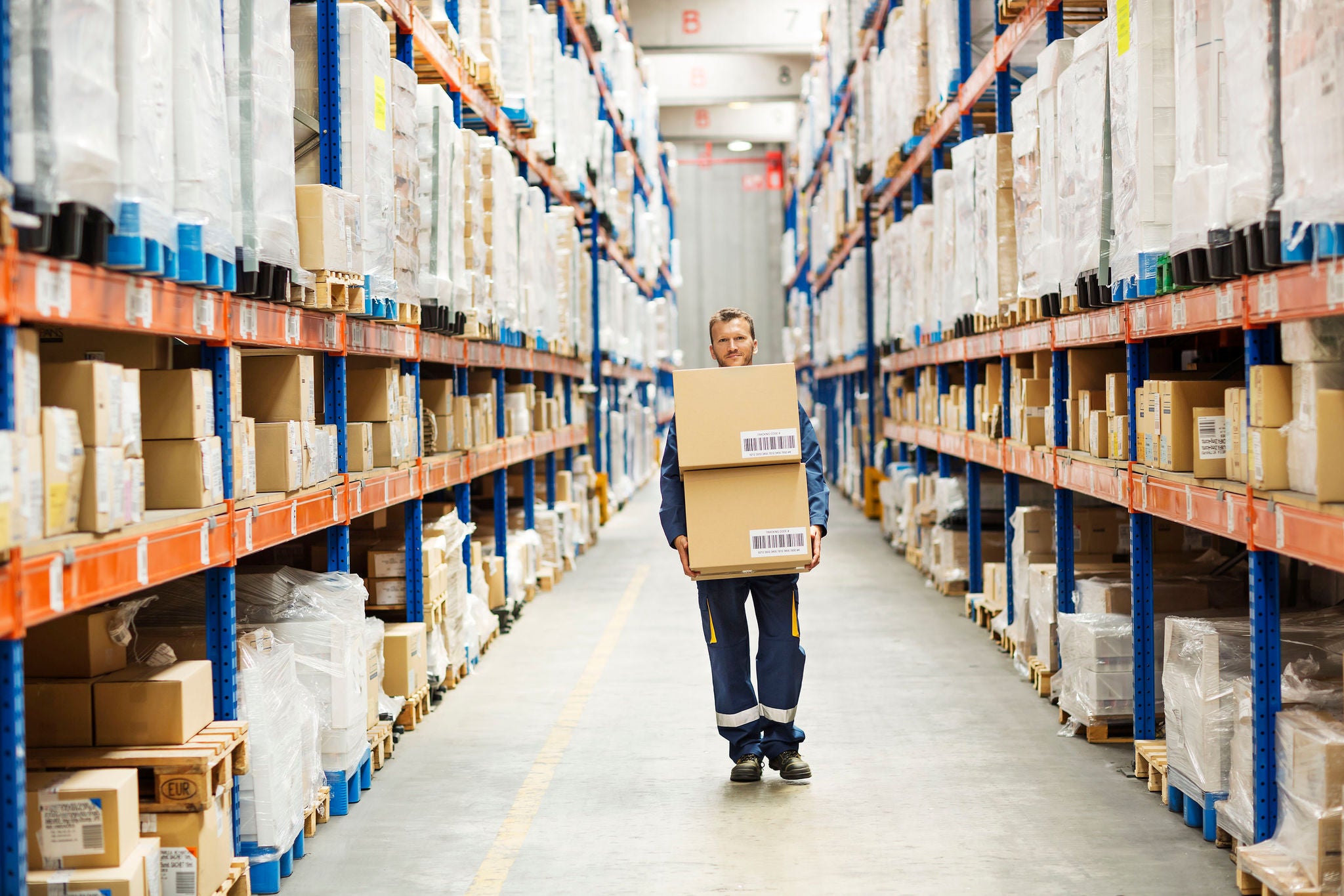 Full length portrait of worker carrying cardboard boxes while walking at distribution warehouse aisle