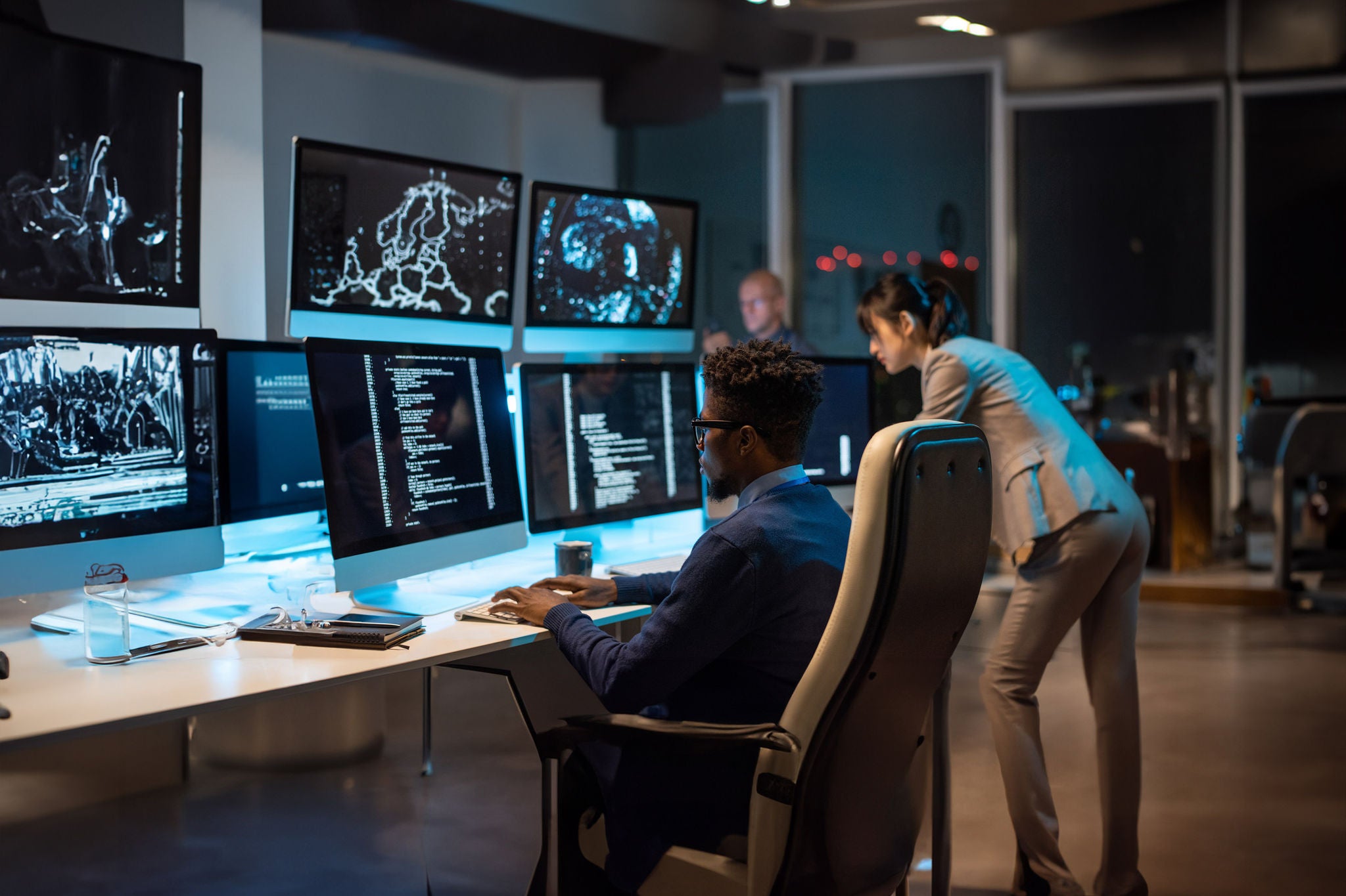 Young it-engineer decoding data while sitting in front of computer monitors and looking at screen of one of them