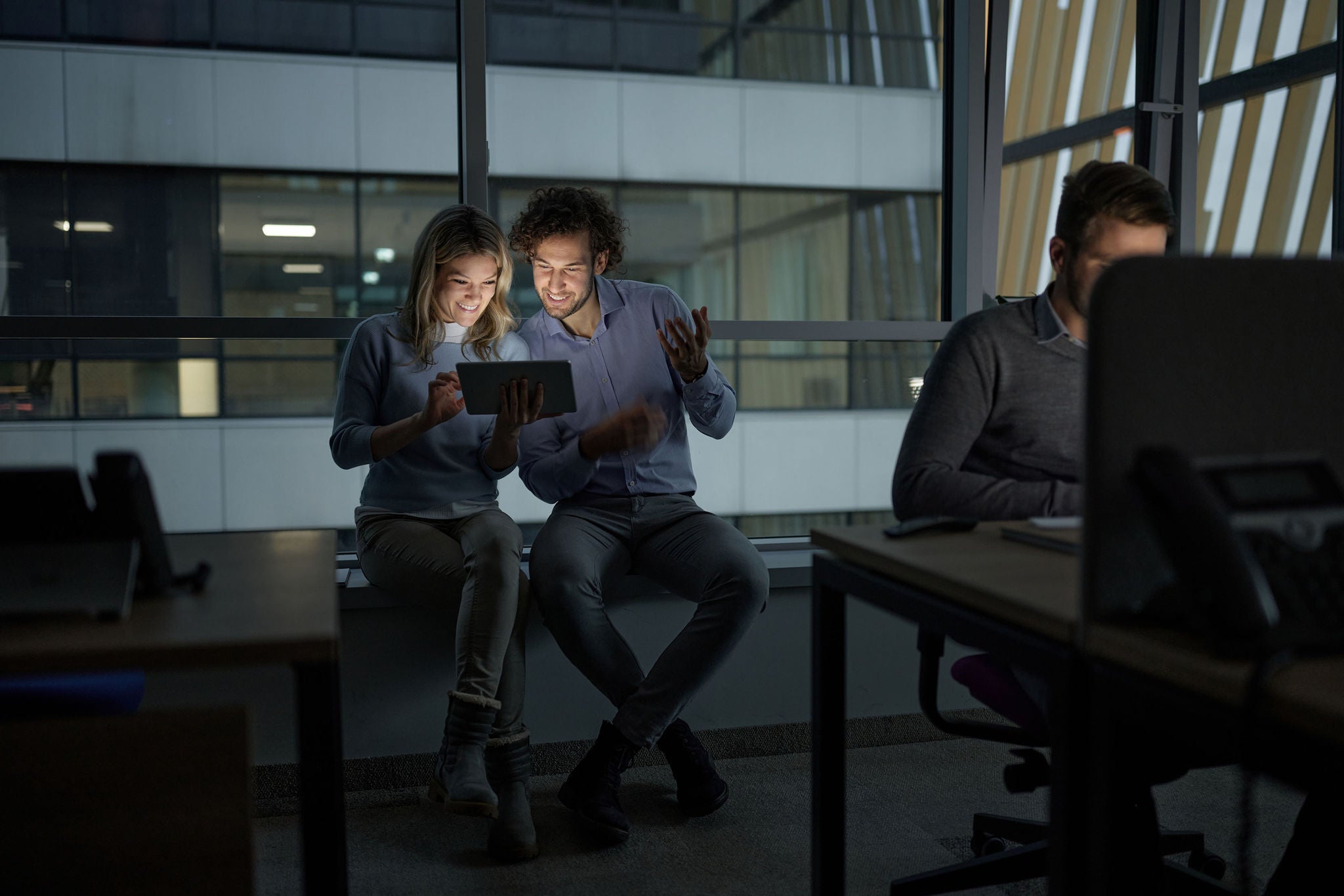 Group of business people working late in the office. Focus is on two of them using digital tablet by the window.