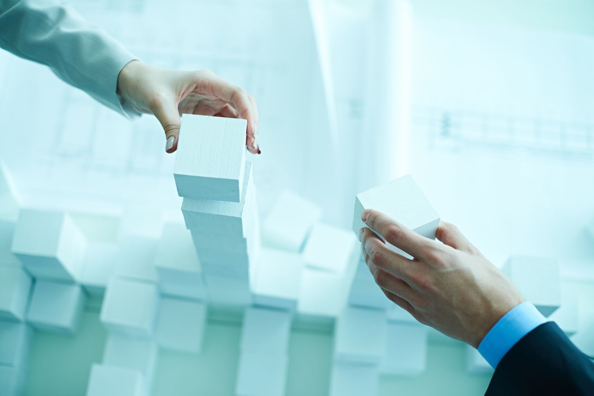 Hands of two business people stacking white toy blocks