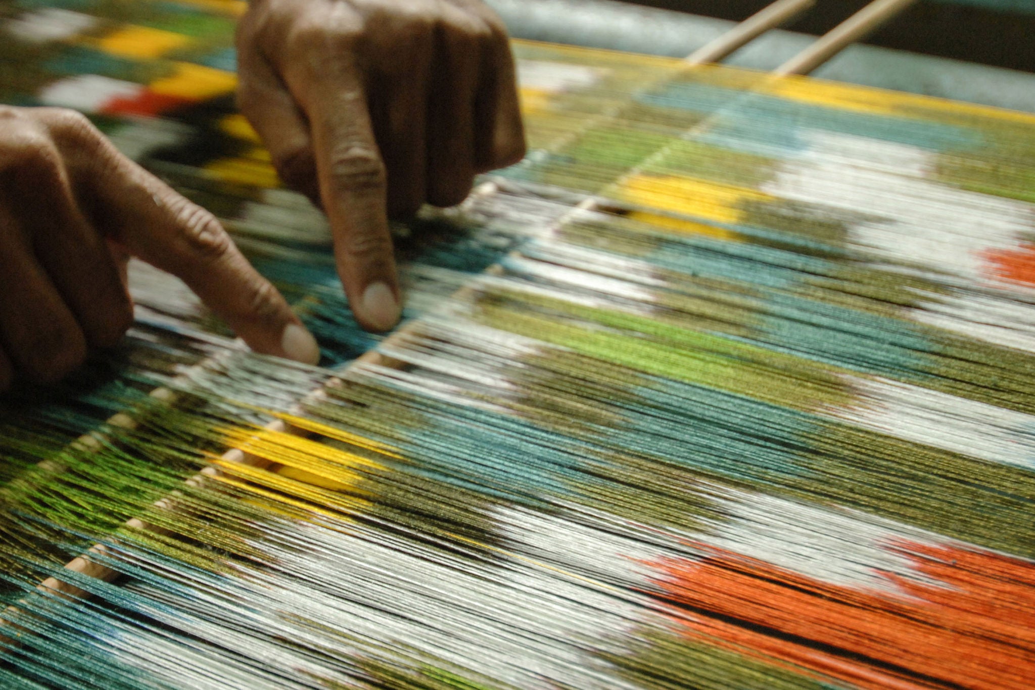 Man's hands behind a loom weaving carpet