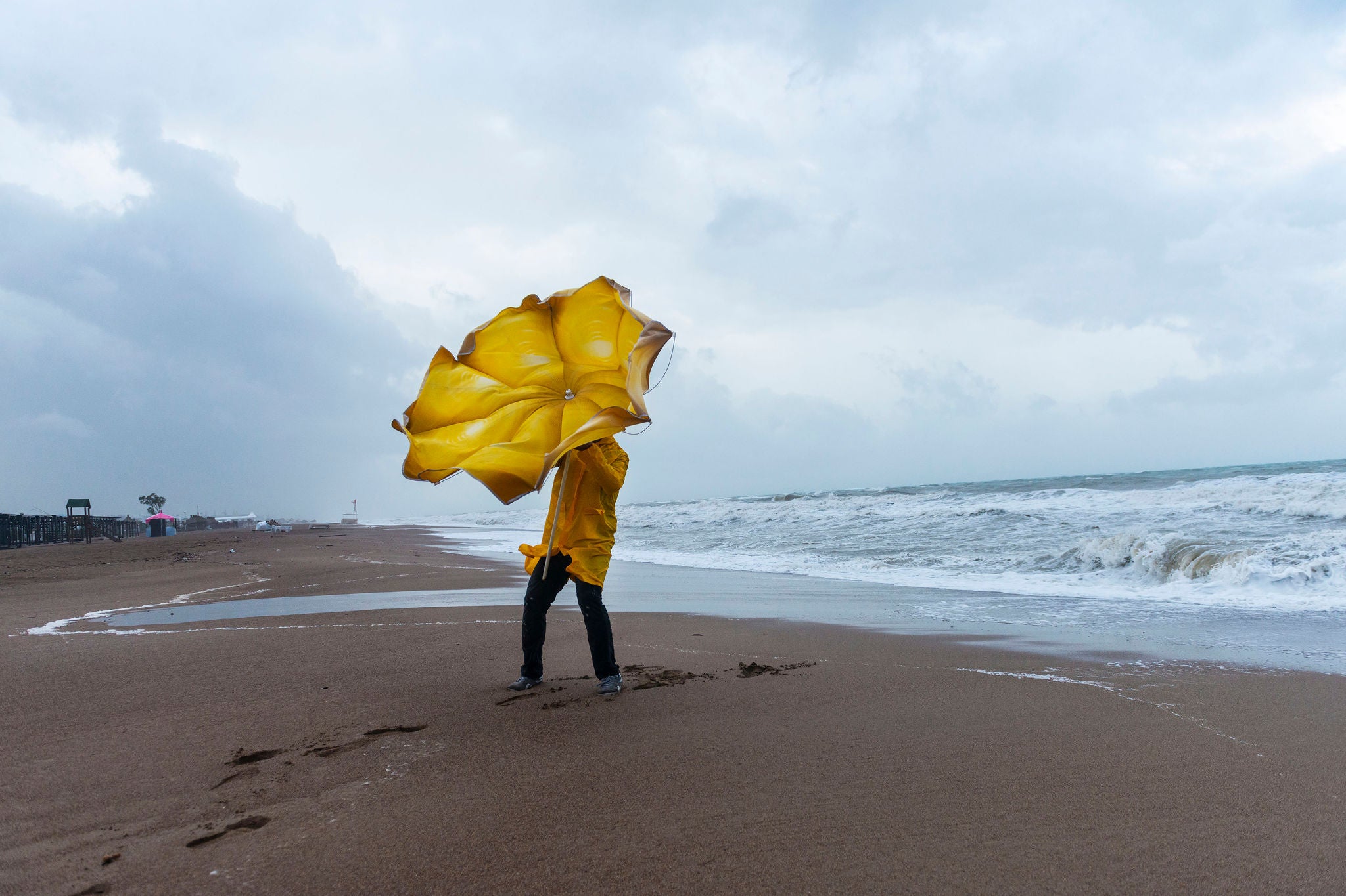 Mand med gul paraply på strand i stormvejr