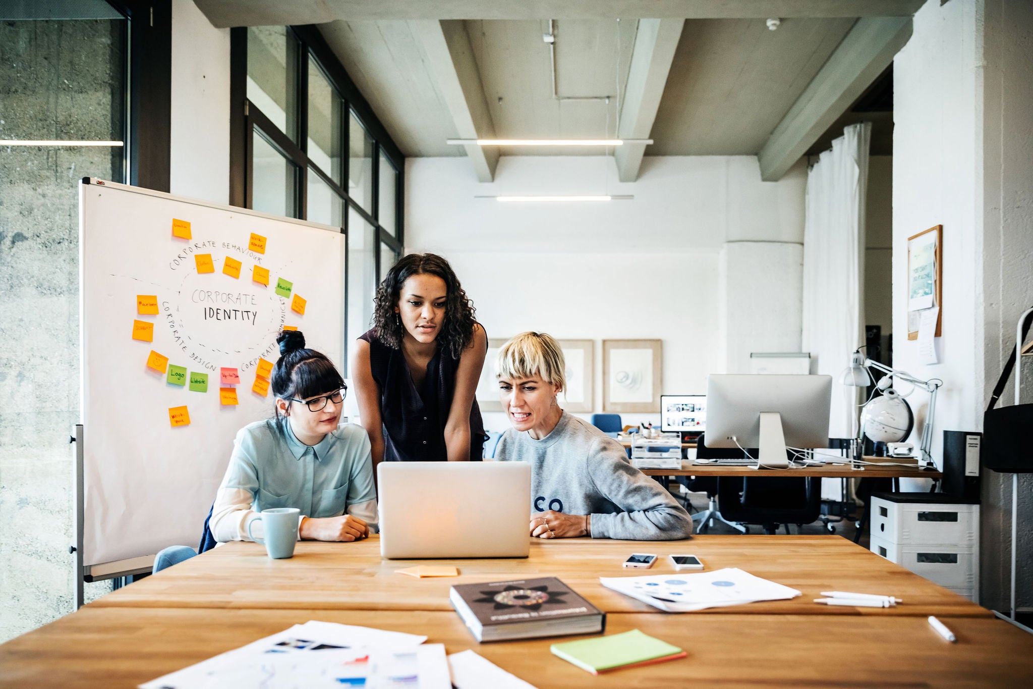 Three casual young businesswomen having a meeting with laptop in a modern office loft