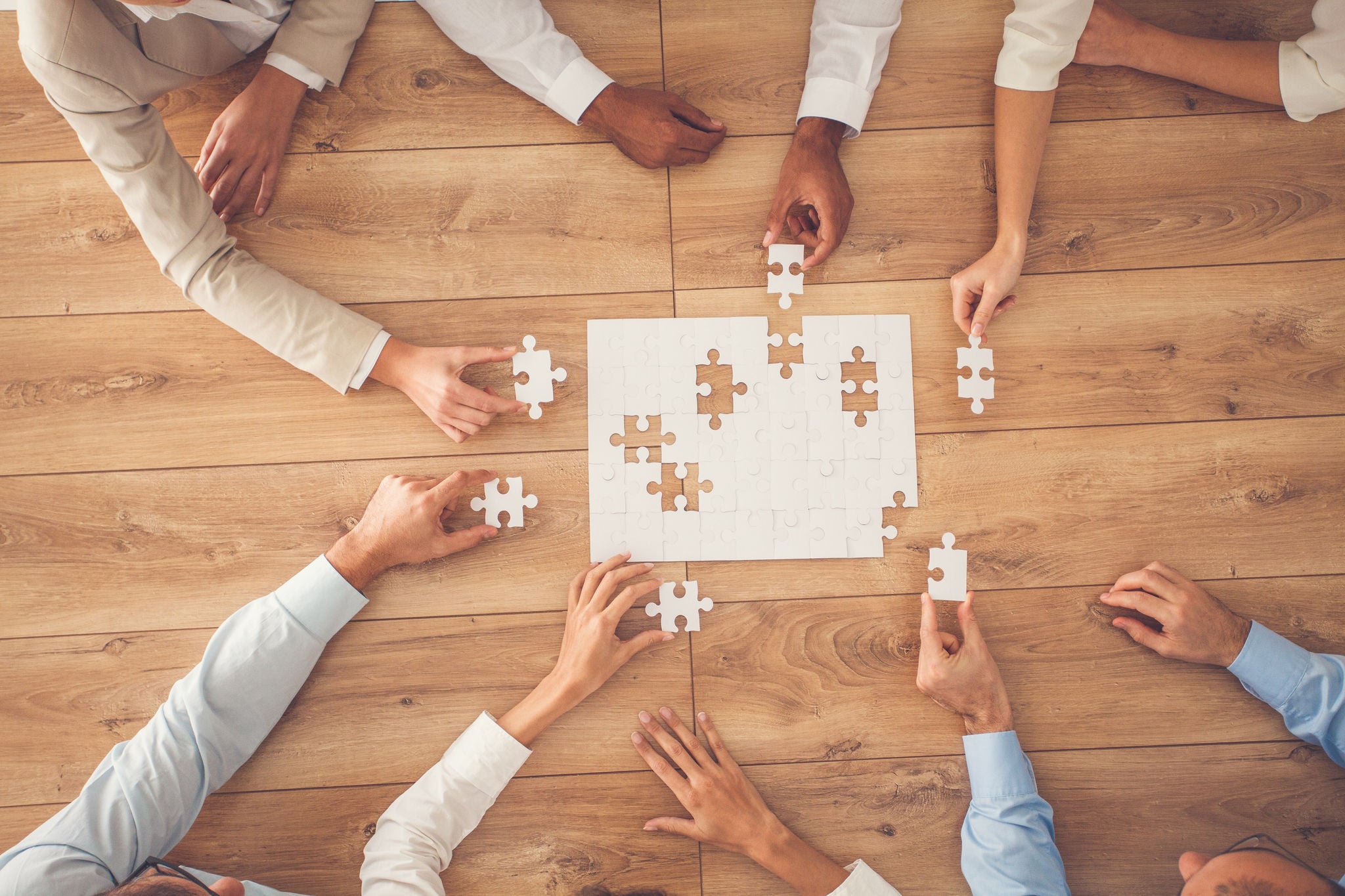 Business people sitting at office desk, putting puzzle pieces together, finding solution, high angle view.