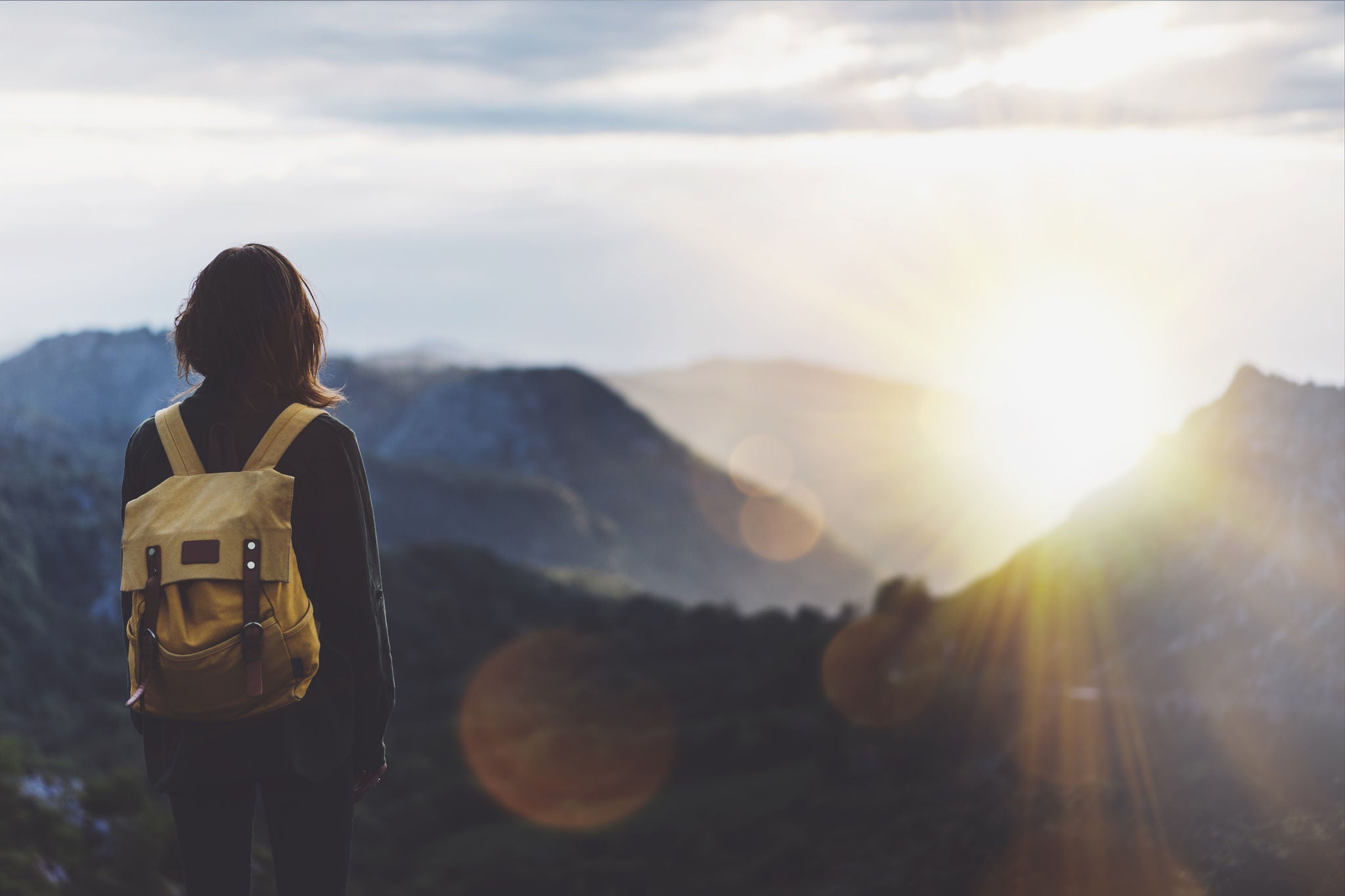 Photograph of a hiking girl looking at mountains and the sun