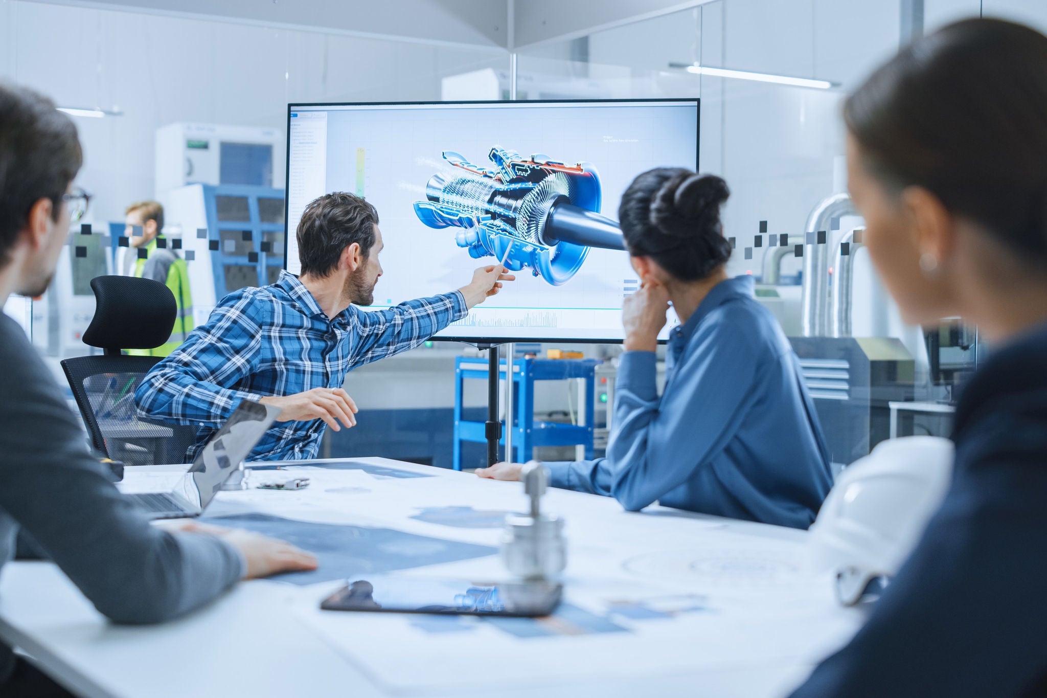 Team taler sammen rundt om et konferencebord med interaktiv skærm med blueprint.