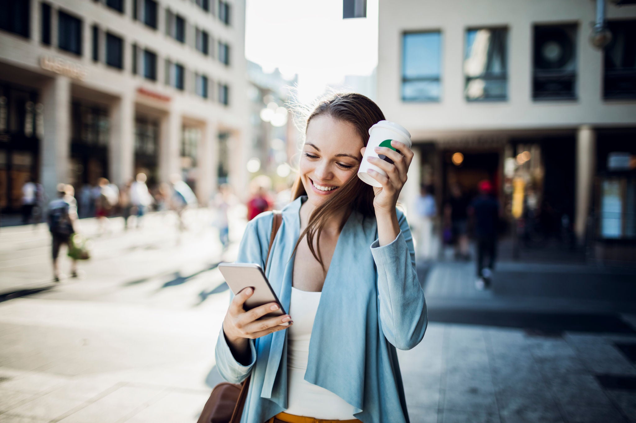 Close up of business woman using a phone while walking and drinking coffee