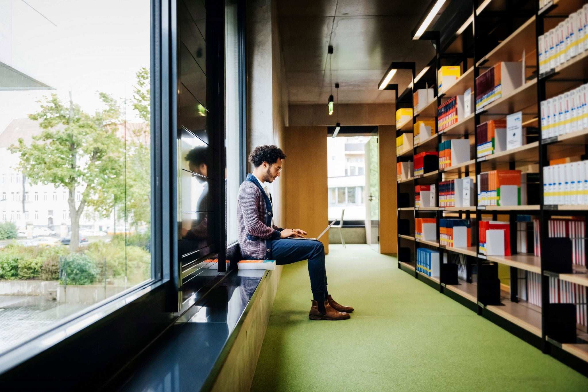 Man Sitting By Large Window Working In Library