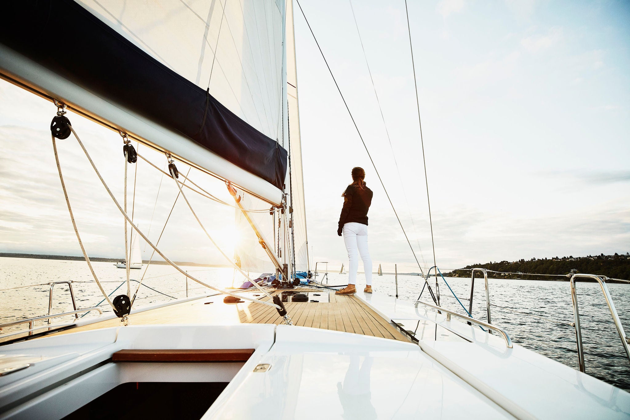 woman stands on foredeck of sailboat watching sunset in summer evening