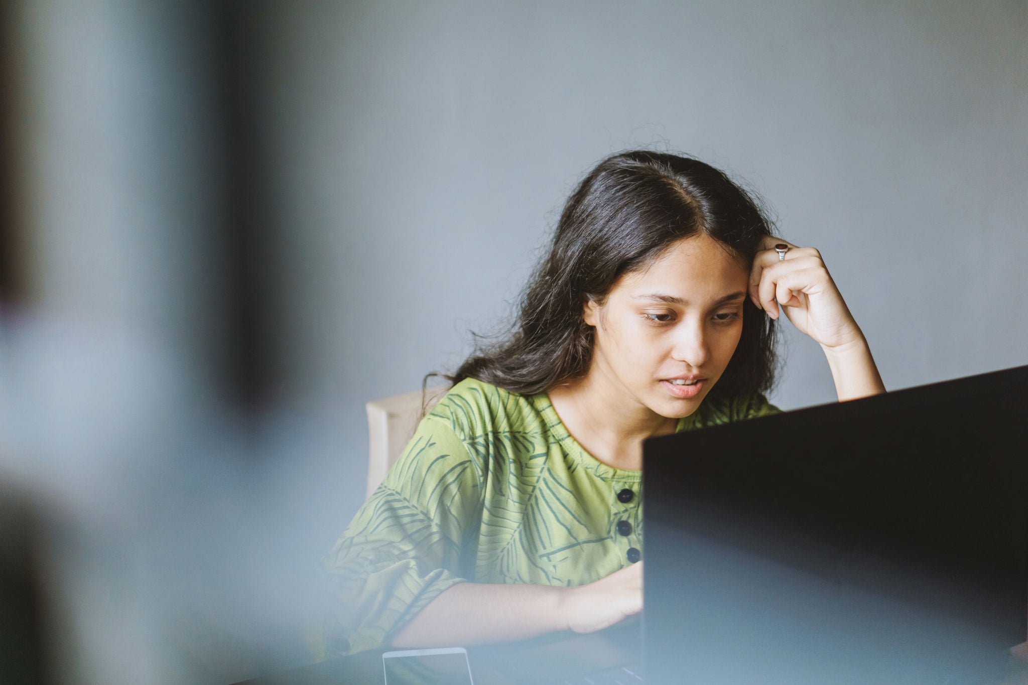 Shot of a Young woman using a smartphone and laptop in her workspace through the window.