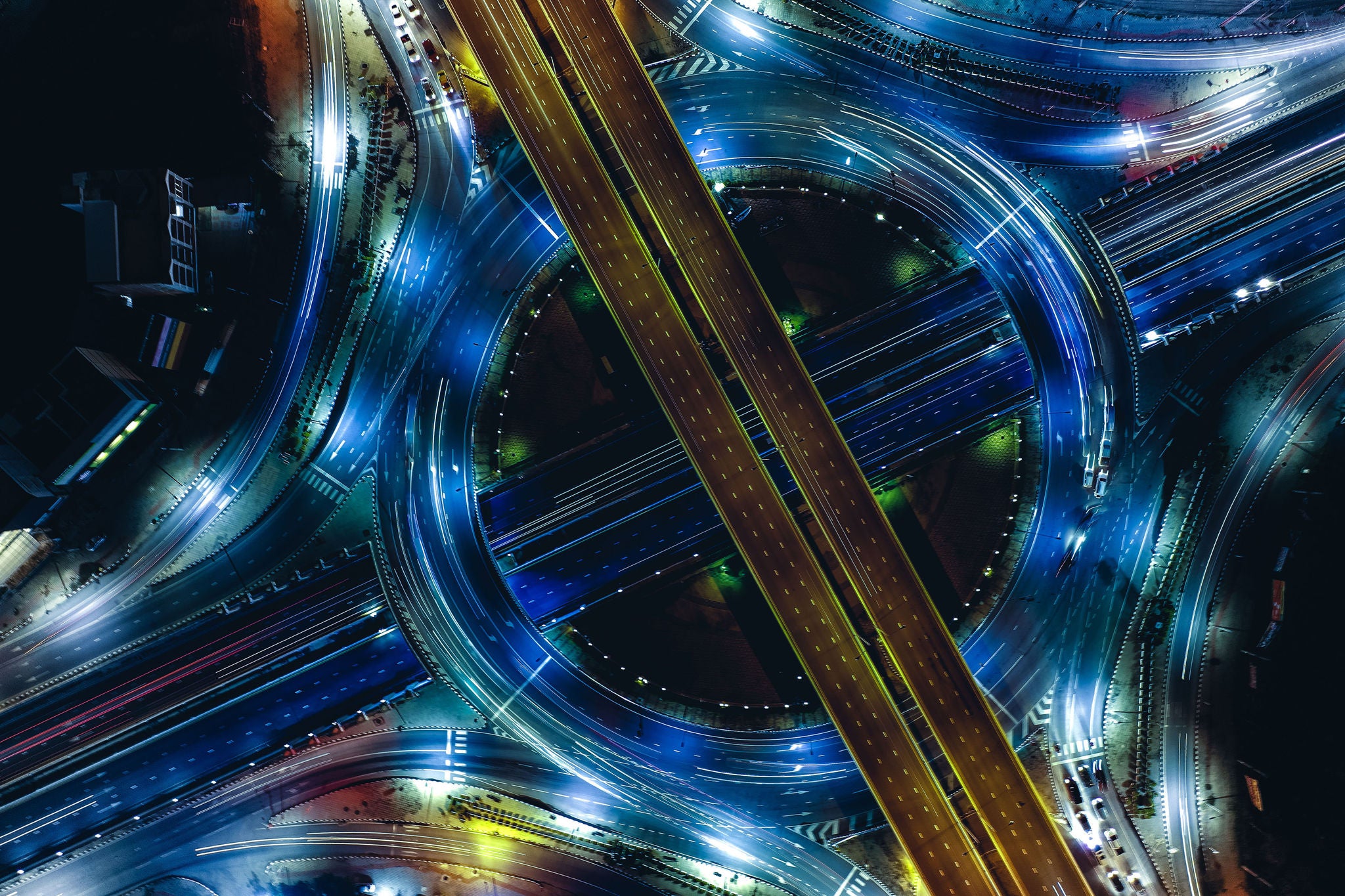 Luftaufnahme einer beleuchteten Autobahnkreuzung mit Lichtspuren bei Nacht.