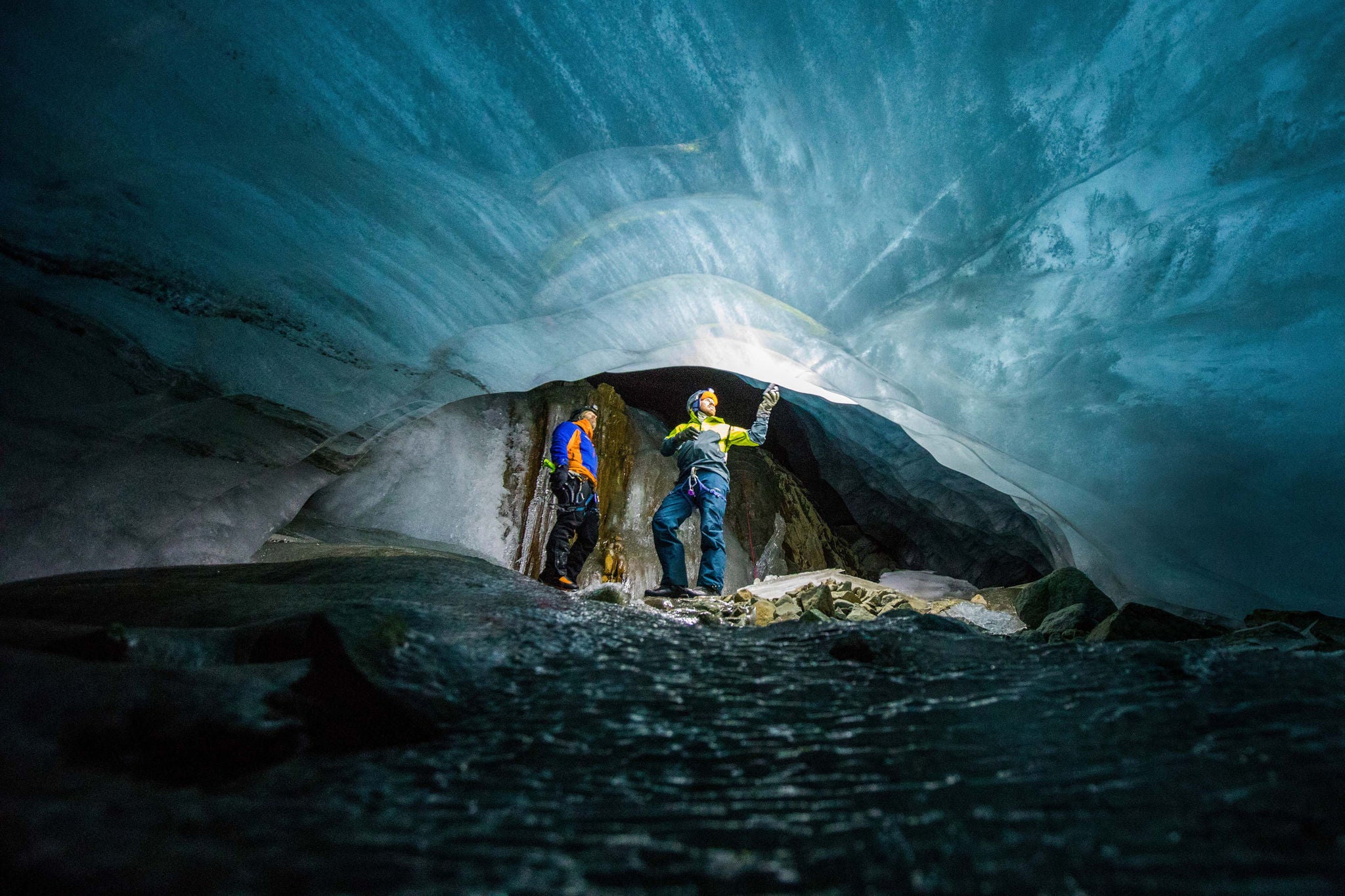 two men marvel at frozen river of ice below a melting glacier