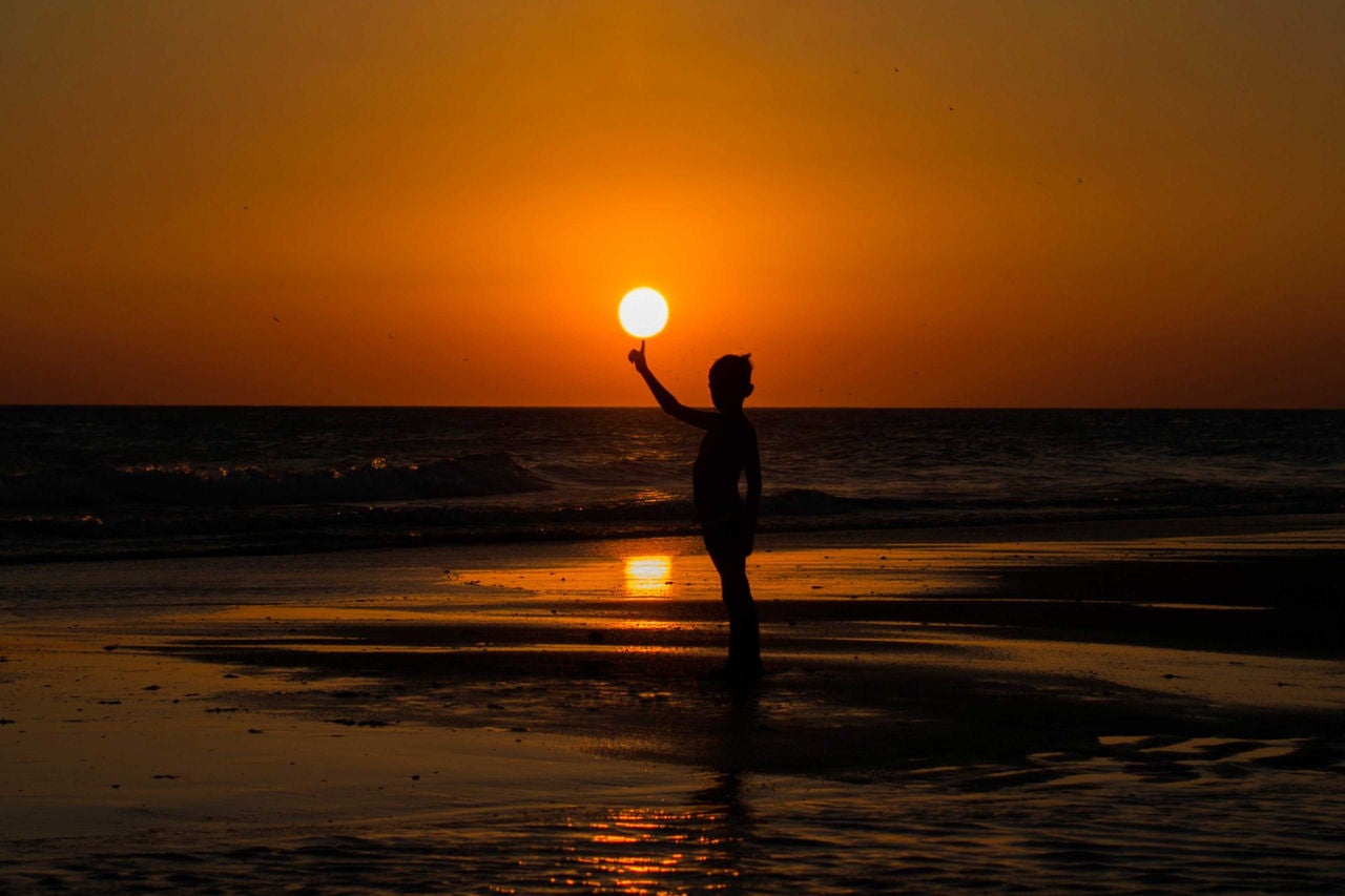 ey-silhouette-of-boy-standing-on-beach-balancing-sun-on-his-finger