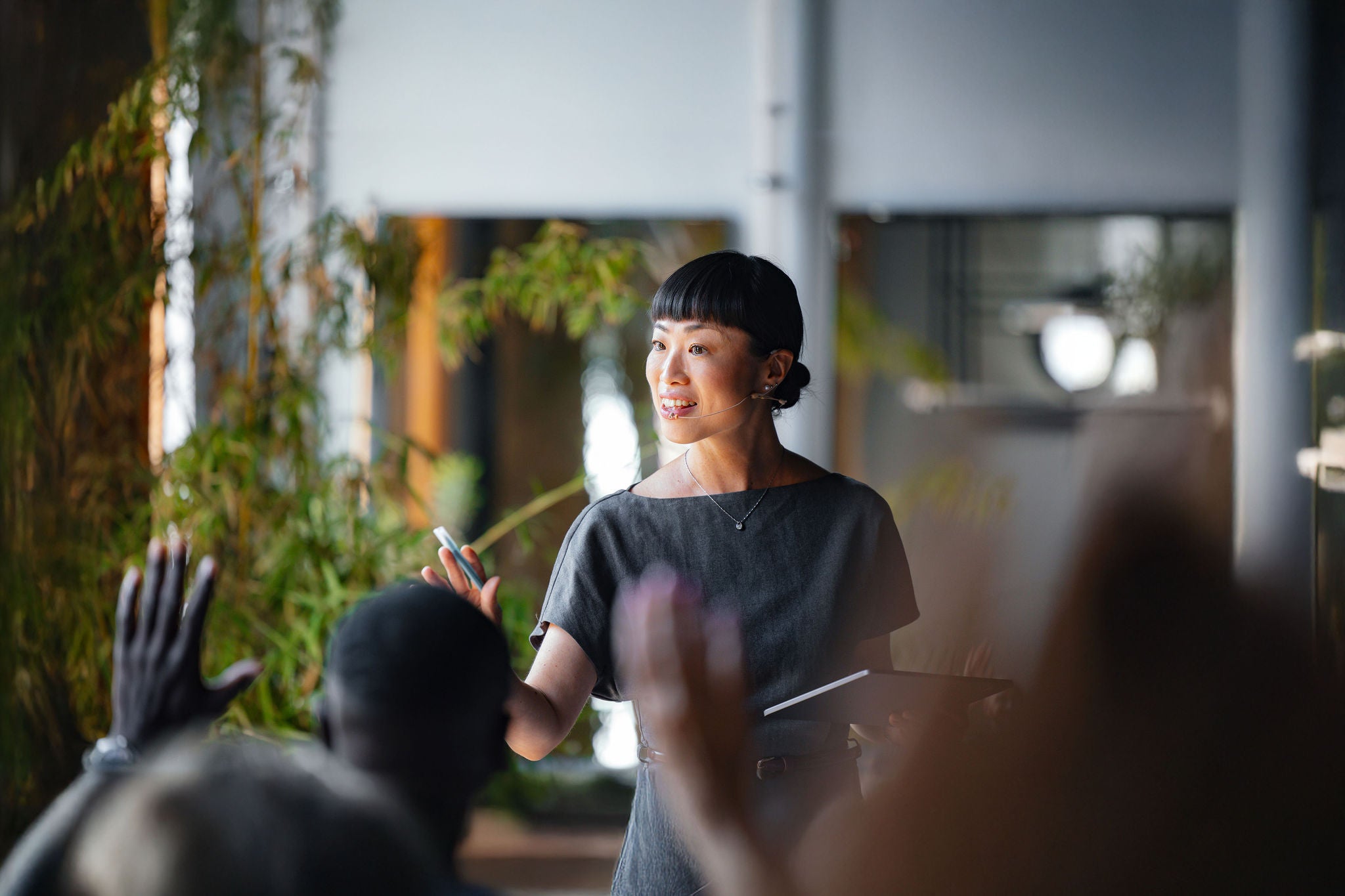 A confident presenter addresses an audience during a business seminar, highlighting her engaging speech. The enthusiastic participants raise their hands for questions.