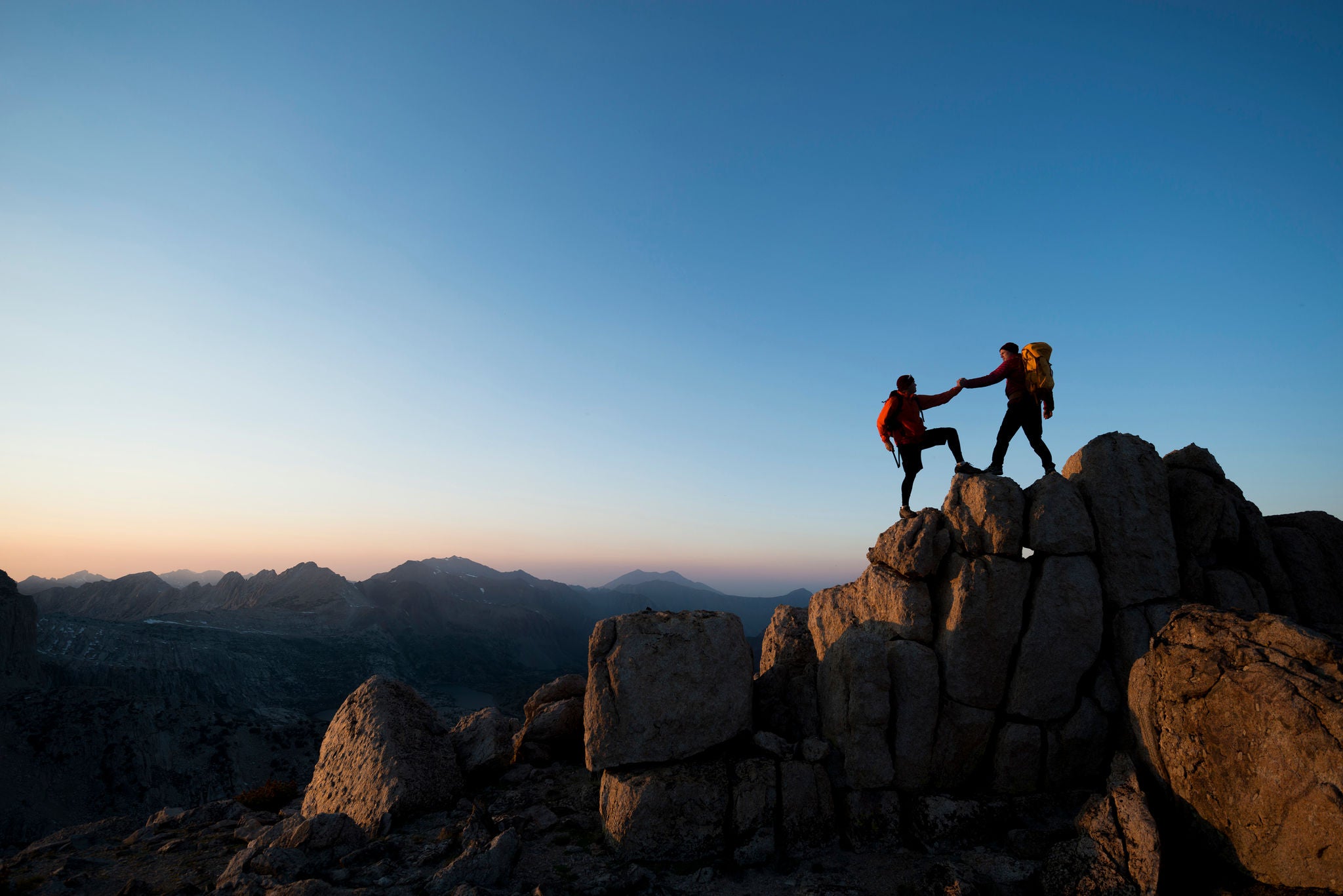 Two climbers helping one another to the summit of a pillar 