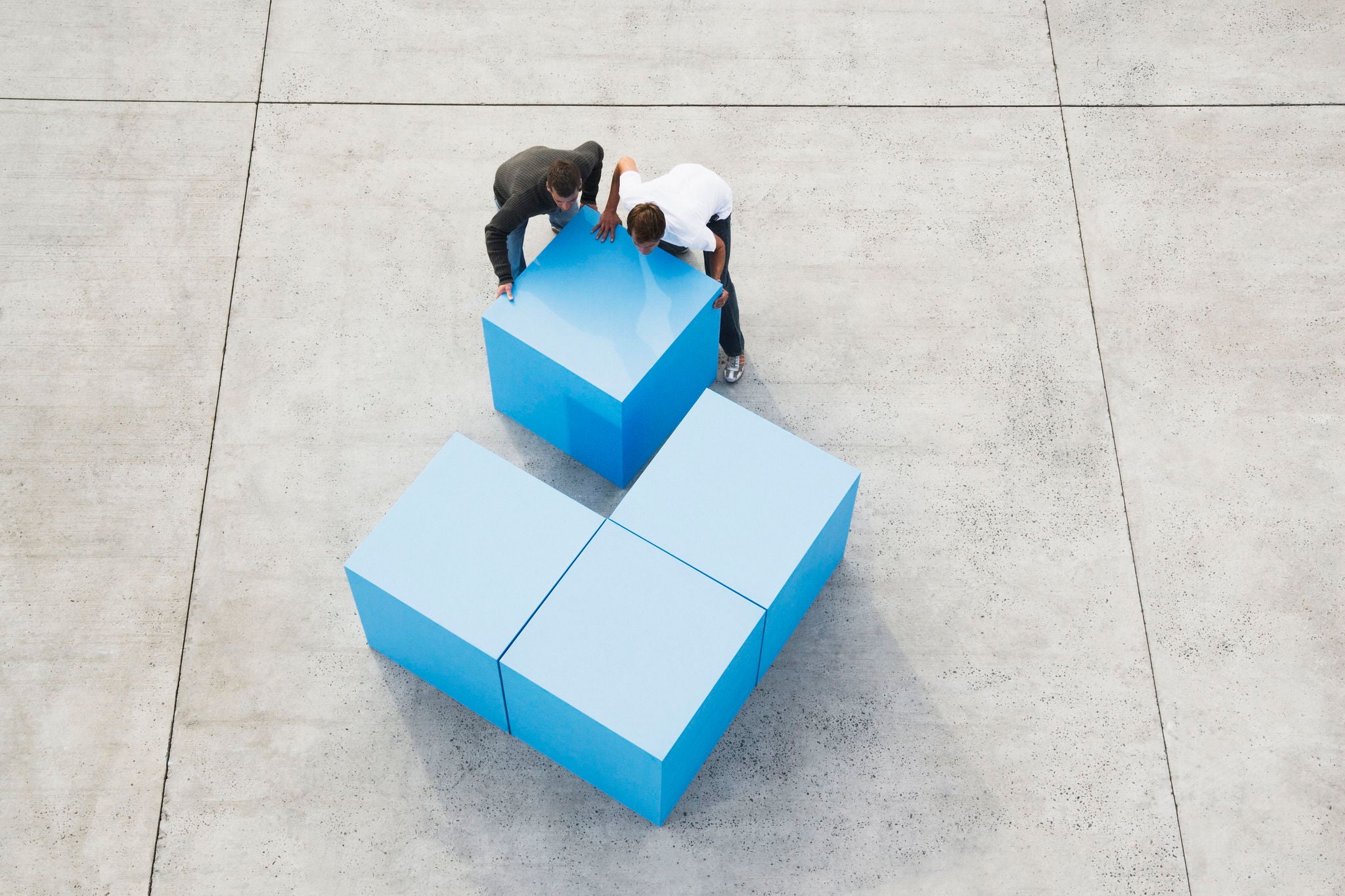 Two men moving large blue block, elevated view