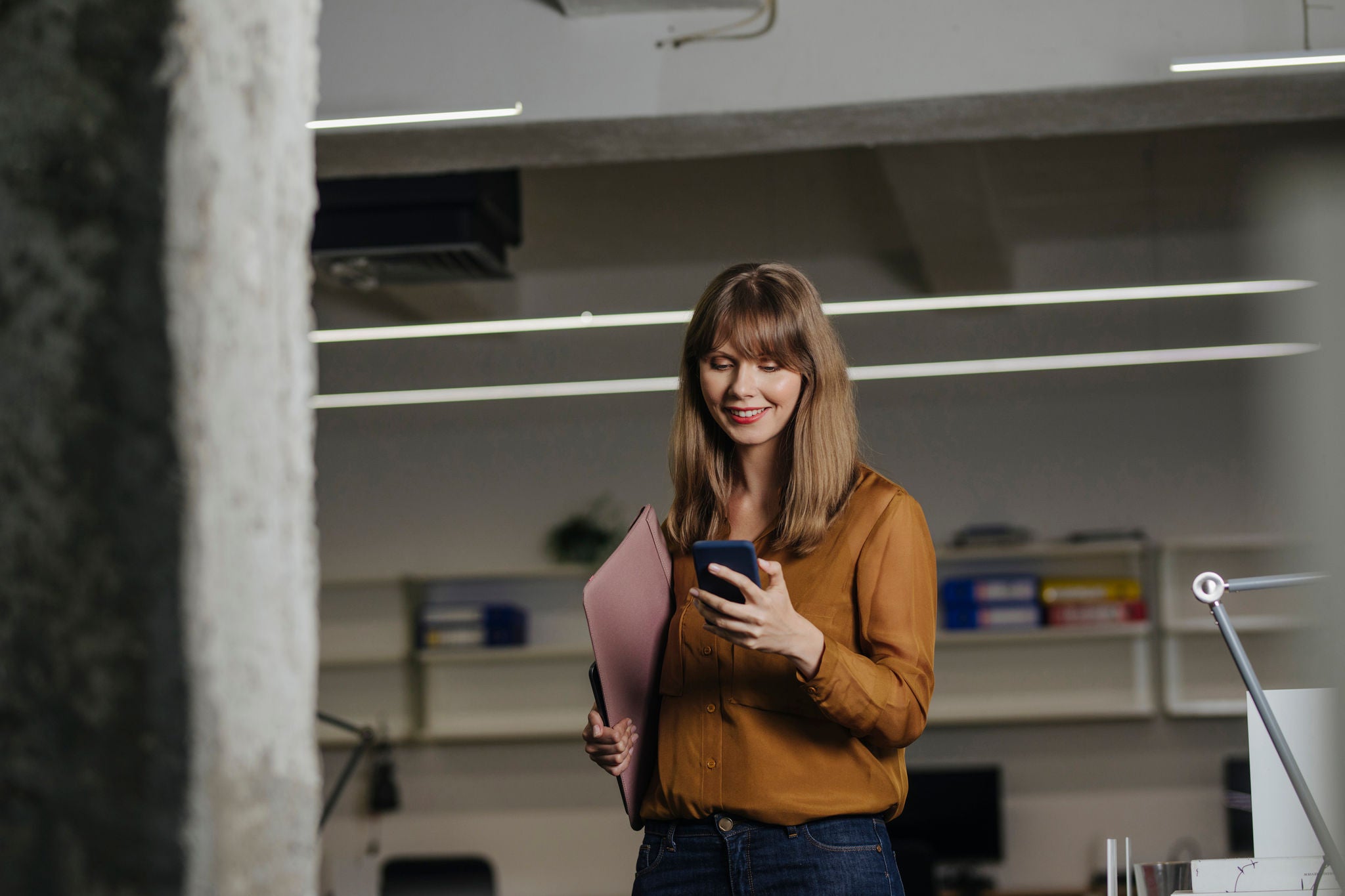 Casually dressed young woman using her mobile phone to read something at work