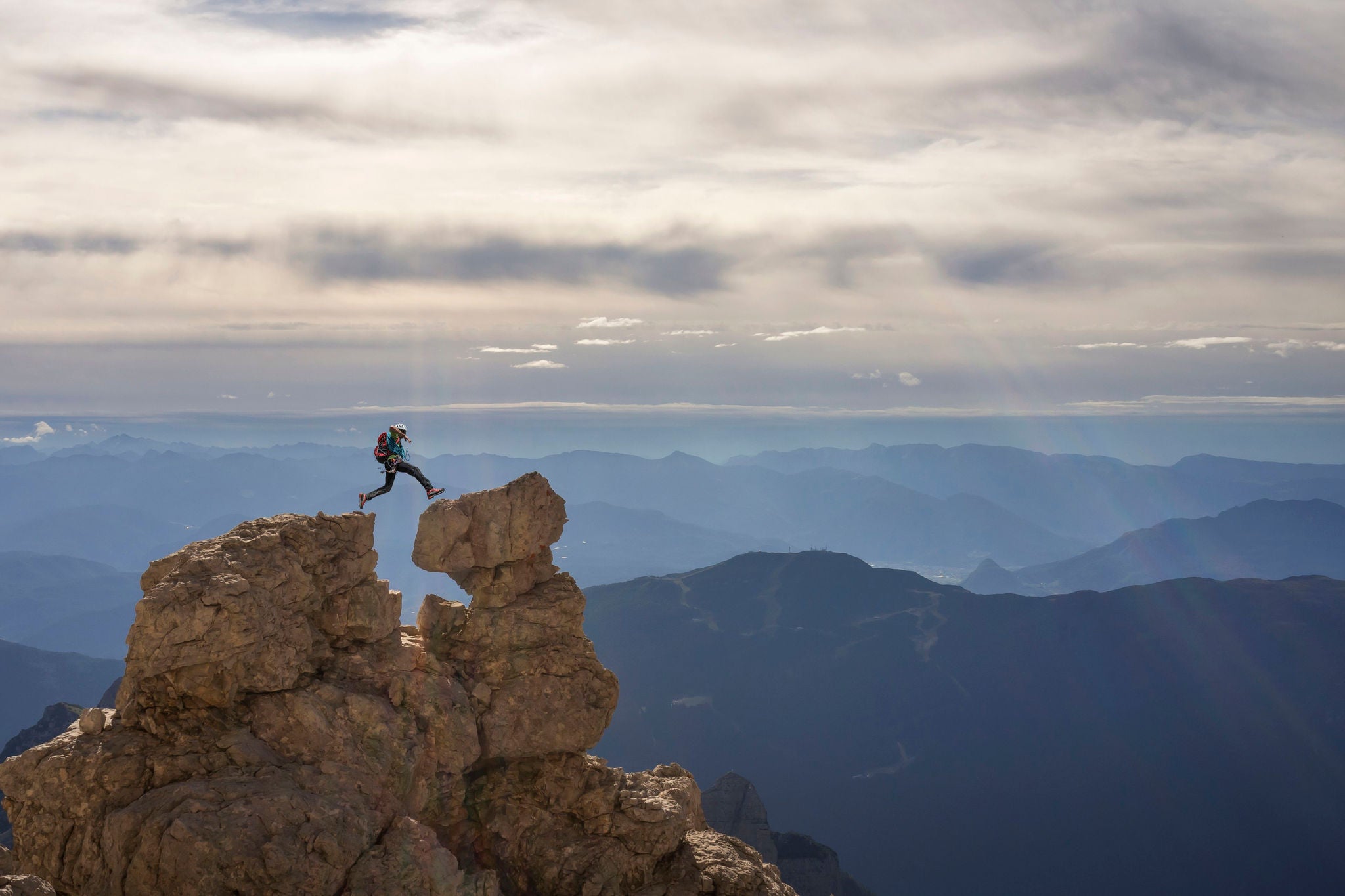 Side view of a caucasian climber jumping between two rocks on the top of a peak in the Dolomites