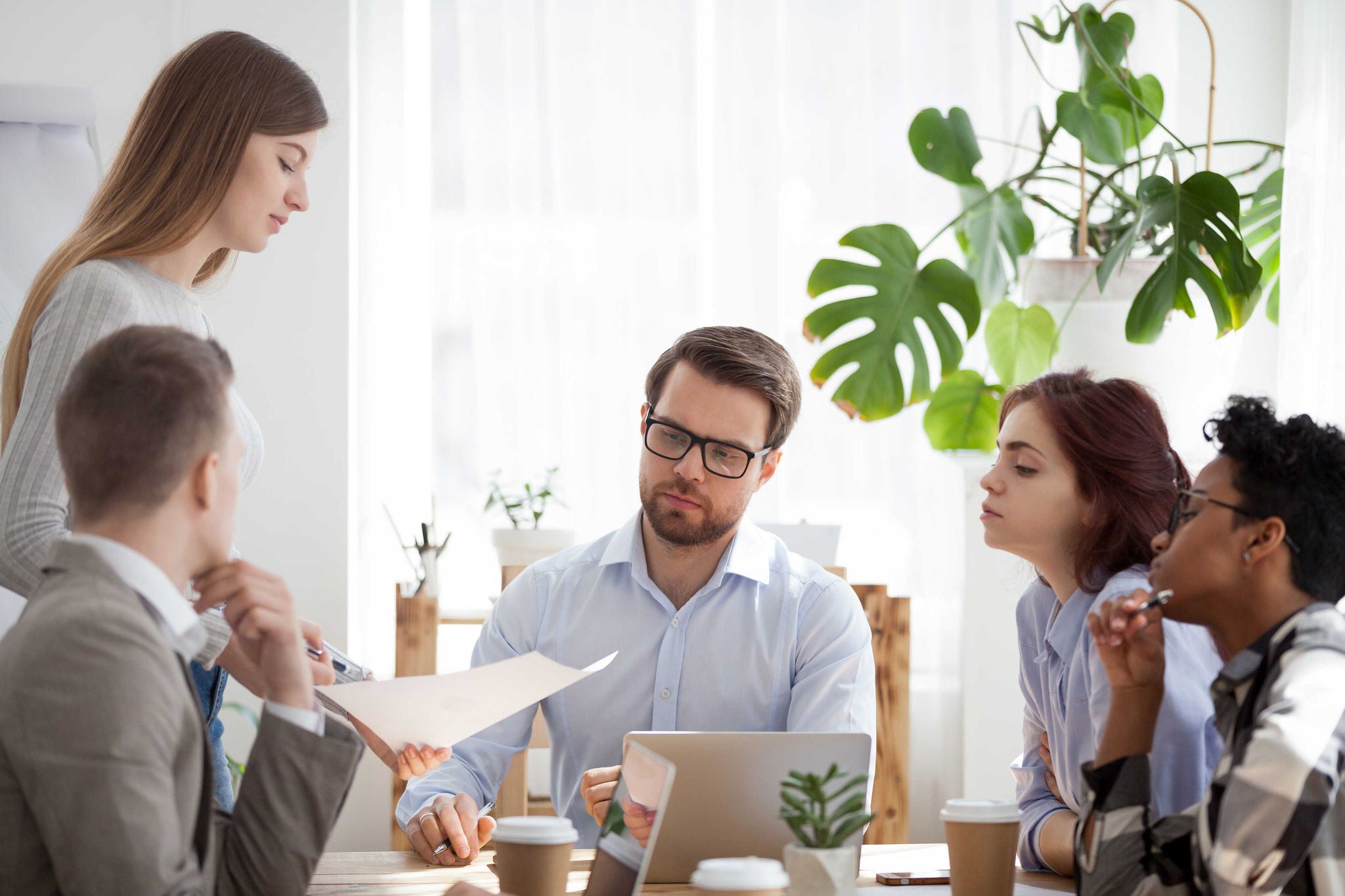 Diverse millennial businesspeople company sitting at seminar presentation in office boardroom. Coach leader woman show report sales statistics analysis documentation to colleagues at business meeting