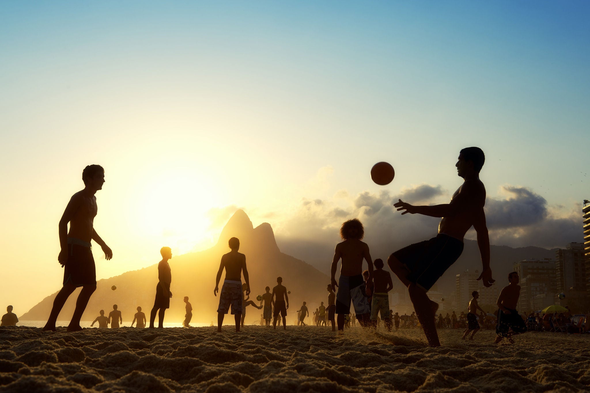 Silhouettes in sunset playing football at the beach