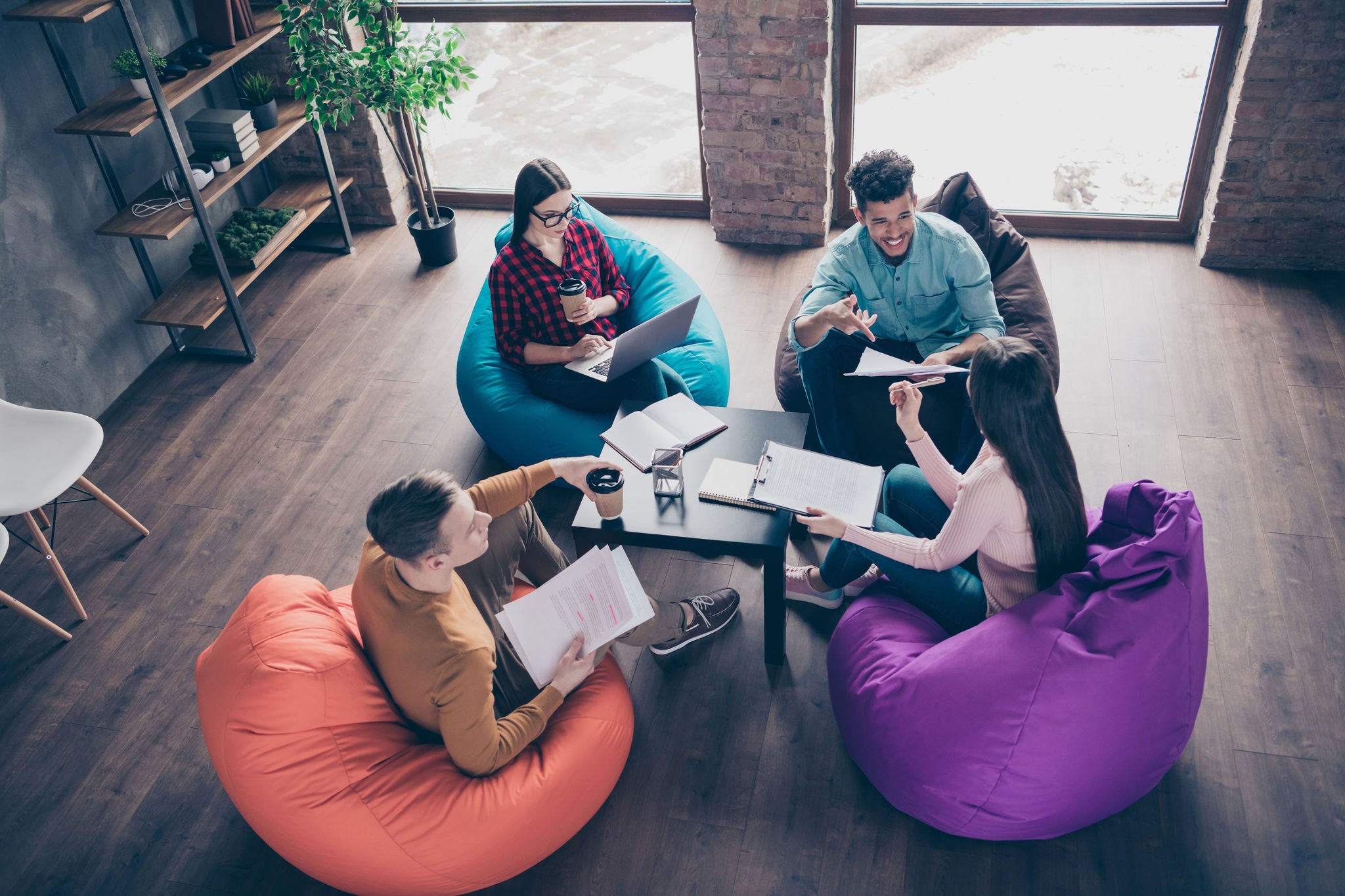 Four individuals seated on bean bags in a modern office setting and having discussion