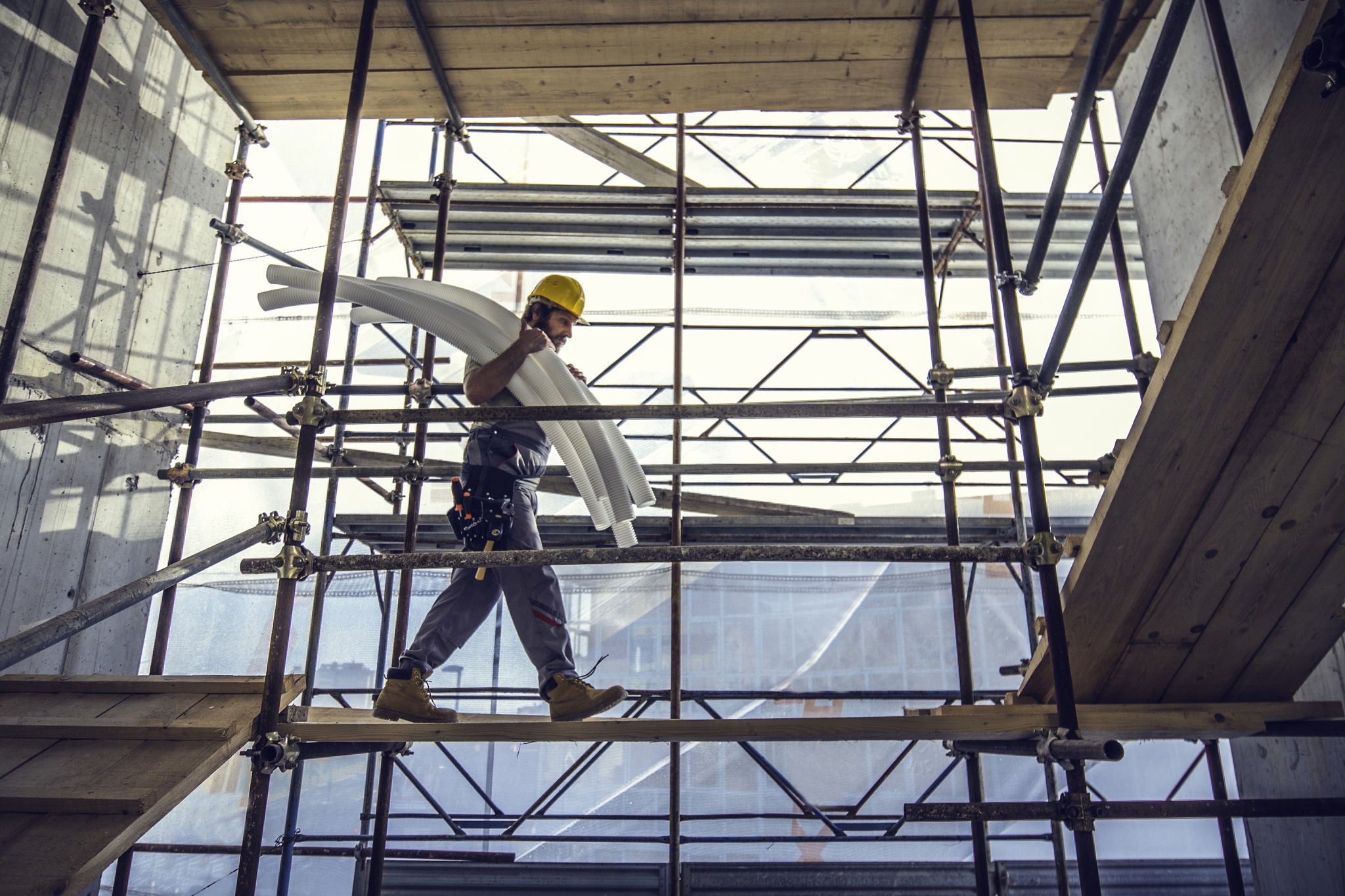 Construction worker carrying pipes