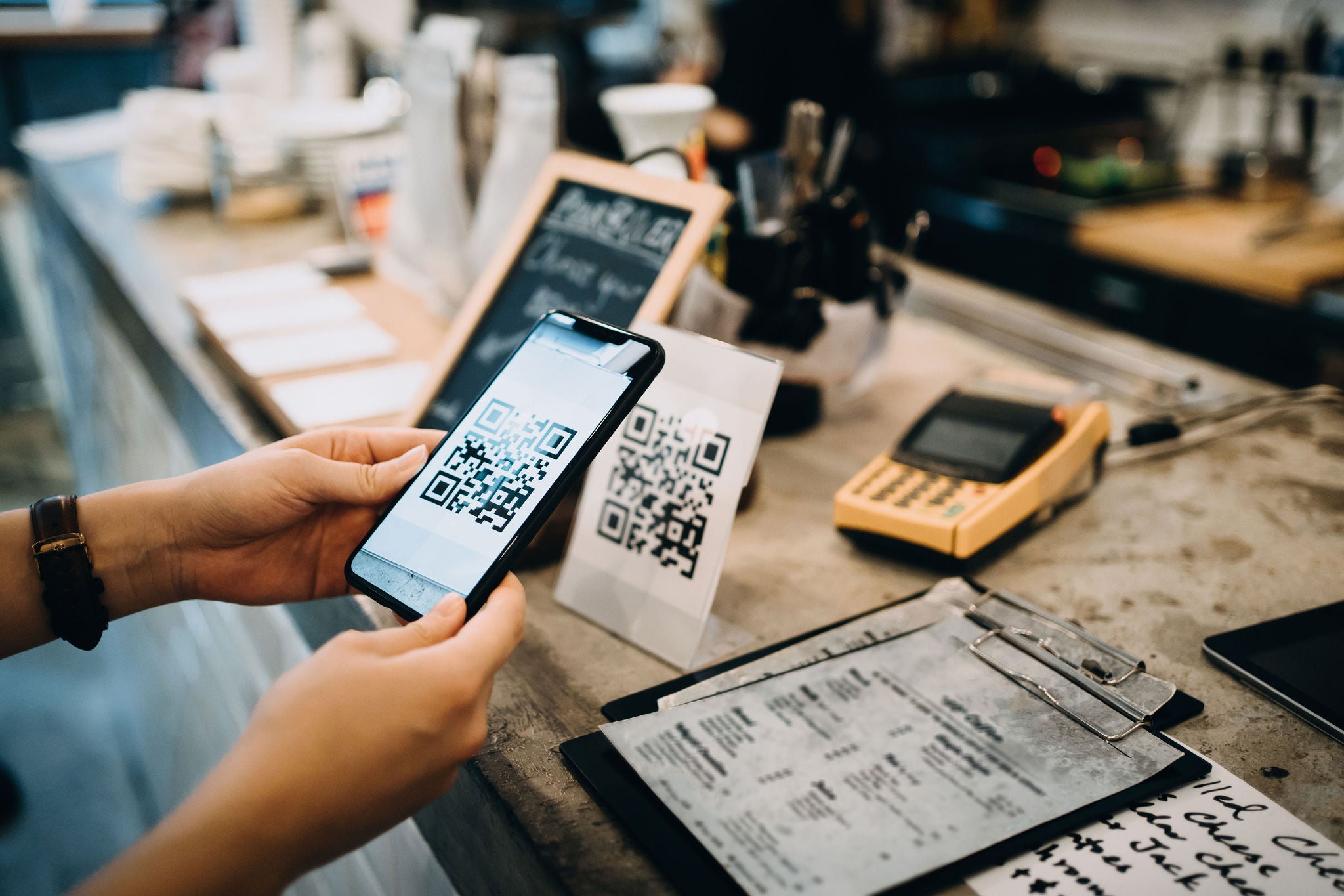 Customer scanning QR code, making a quick and easy contactless payment with her smartphone in a cafe