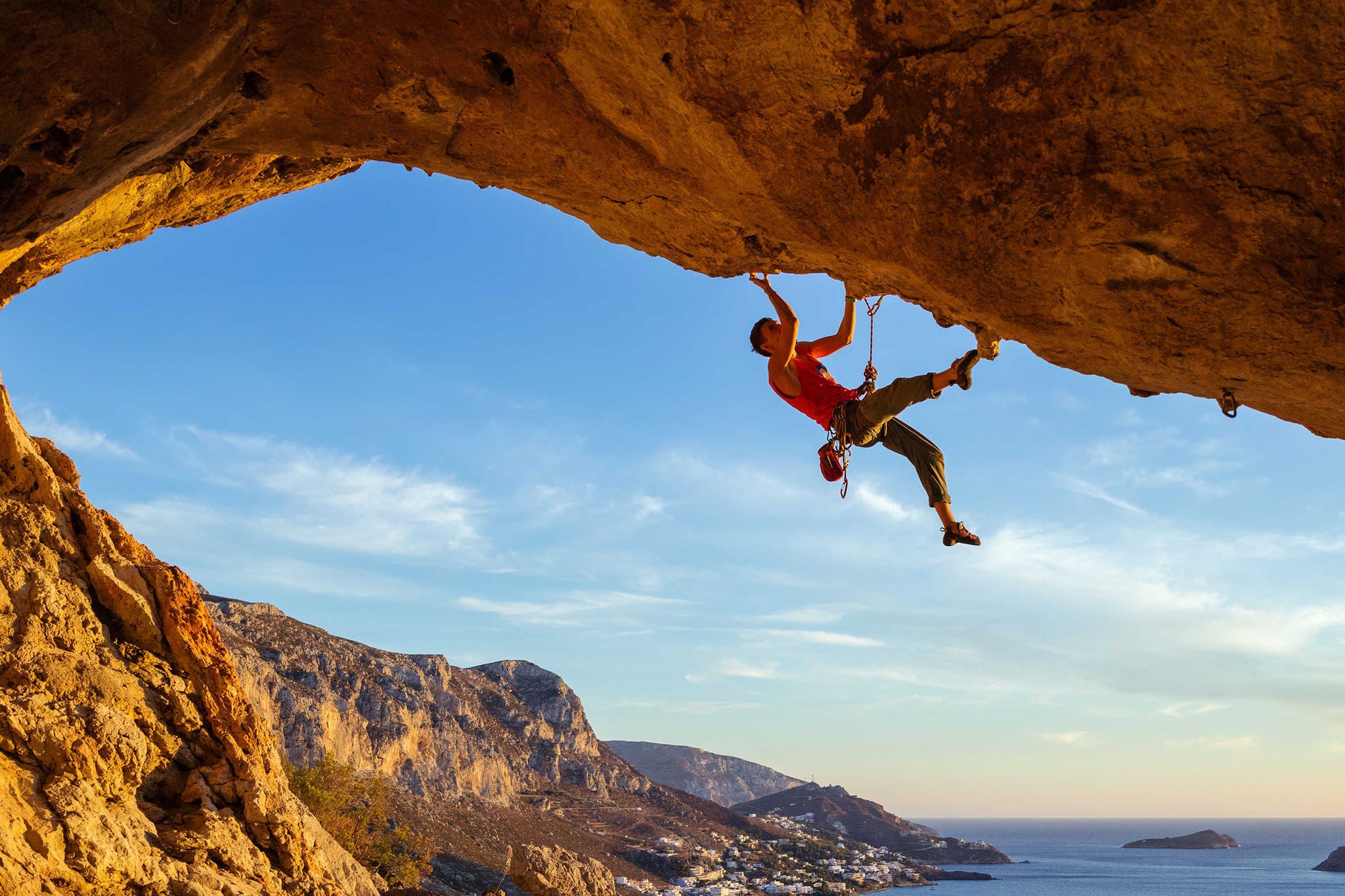 Male climber on overhanging rock against beautiful view of coast below