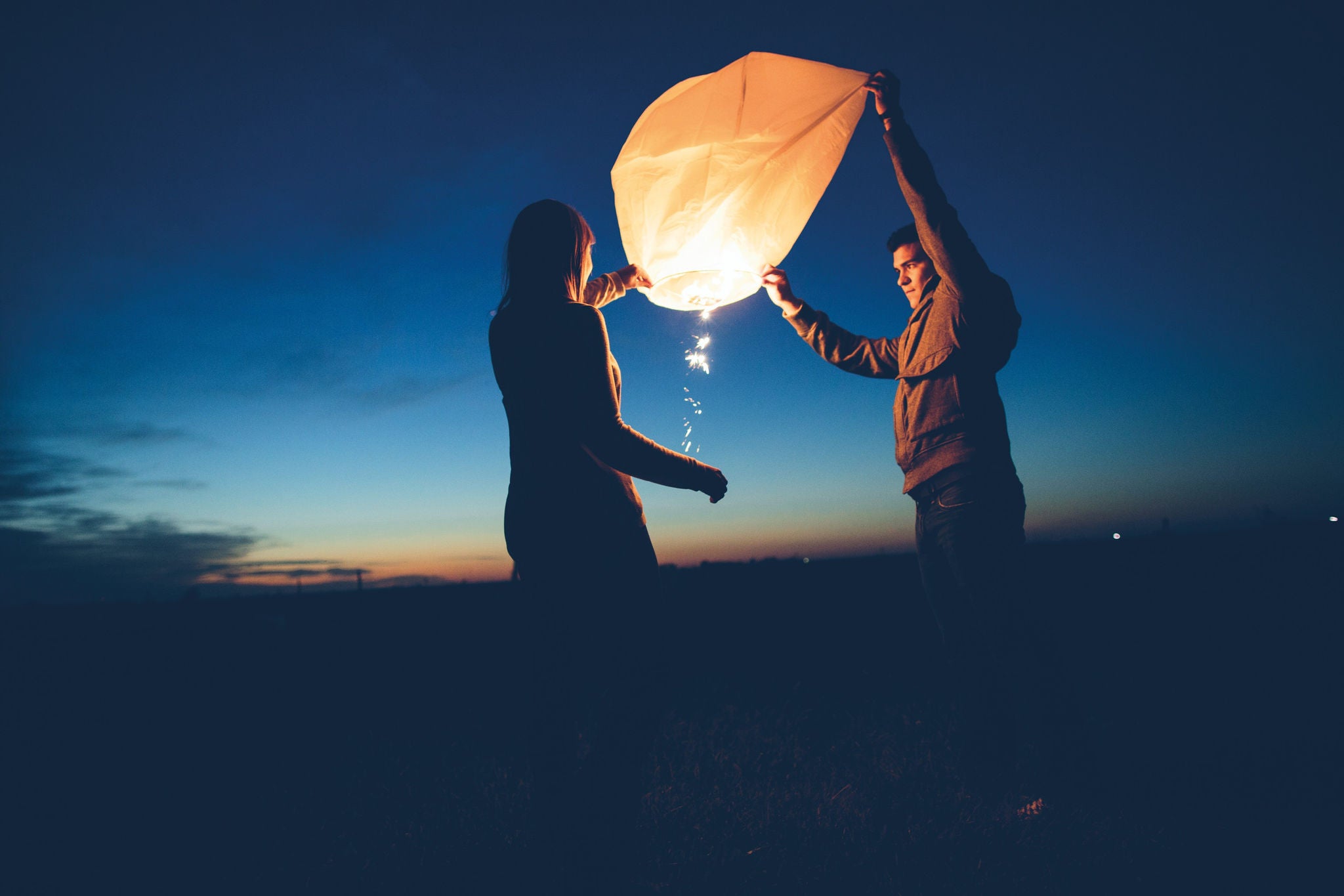 young couple lighting chinese lanterns at twilight