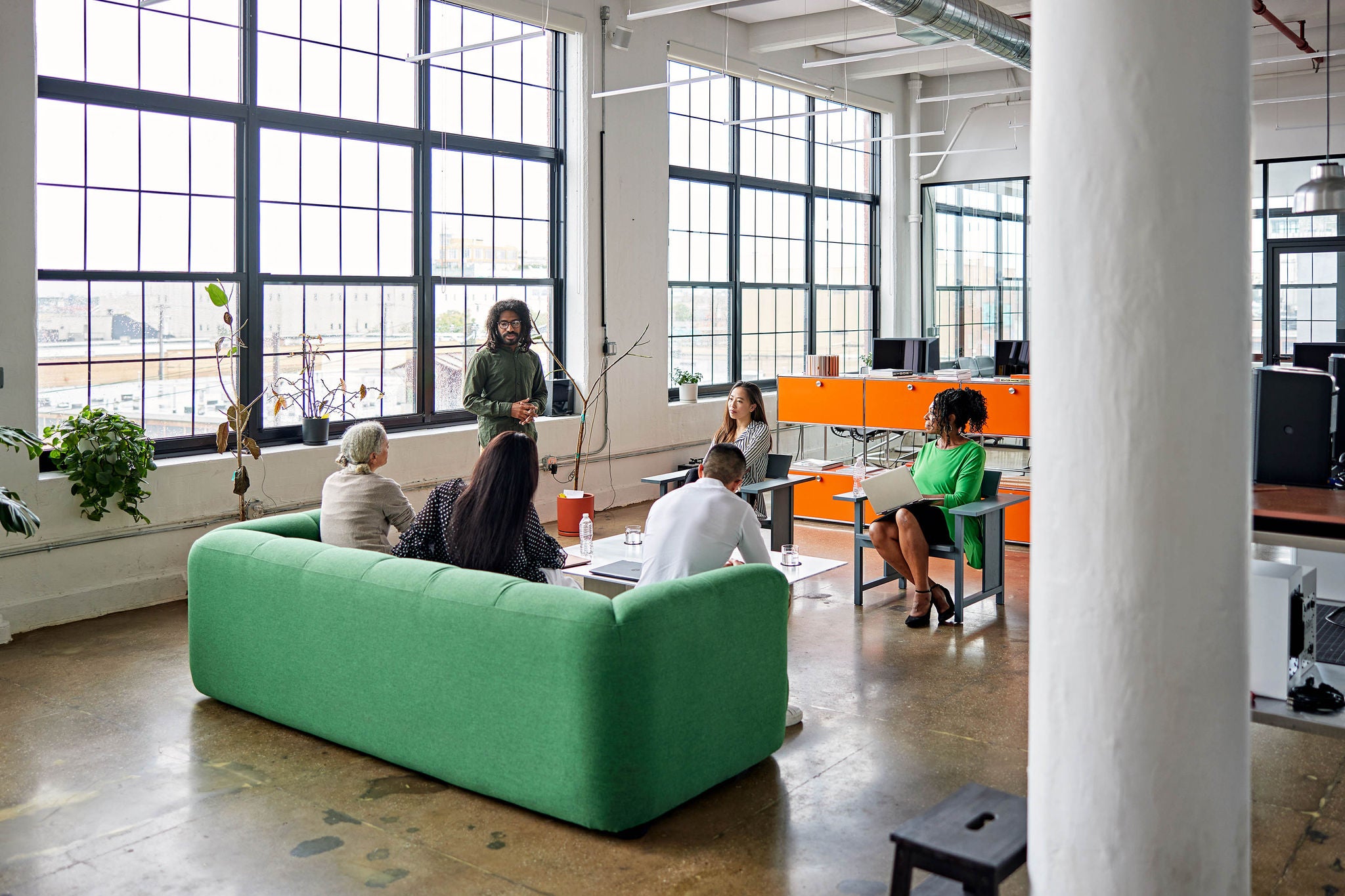 Full length view of creative team sitting in informal meeting area, listening to project manager’s update and discussing plans.